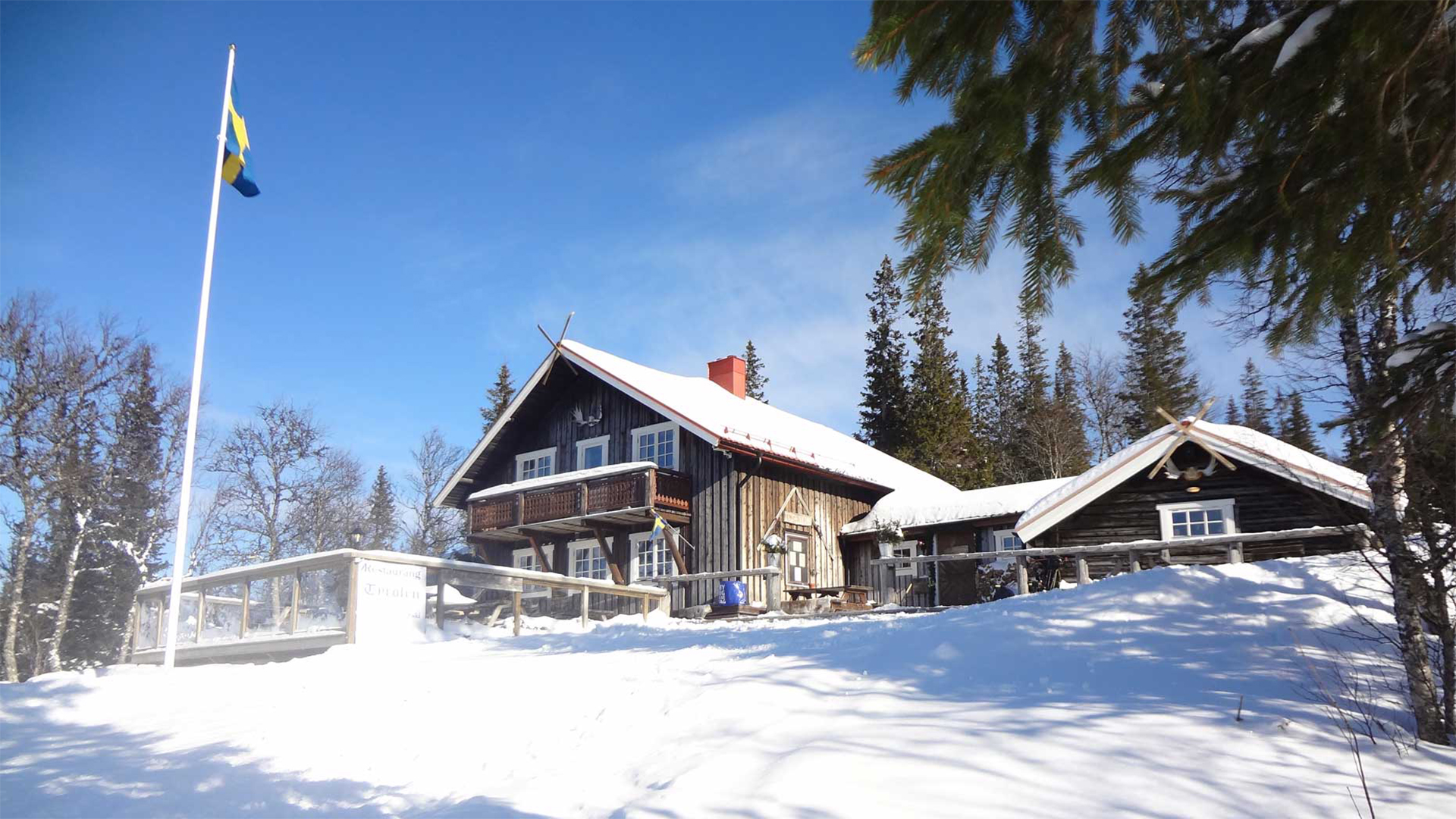 Svensk fjällstuga i vinterskrud med snöklädda omgivningar och hissad svensk flagga