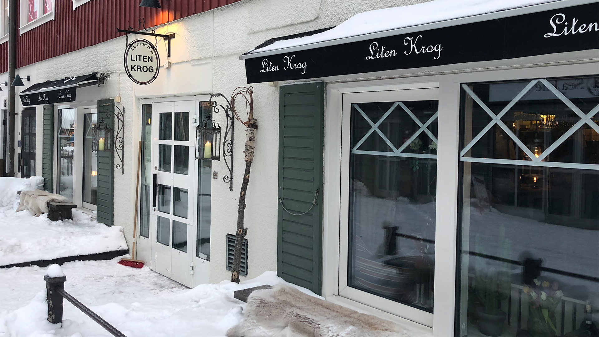 Snötäckt trottoar framför restaurangen Liten Krog med fönster och dörr i en traditionell byggnad