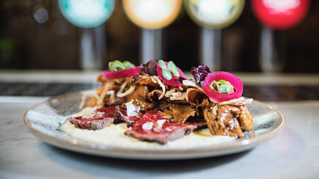 Tallrik med fint skuren biff toppad med picklad rödlök, örter och svamp, serverad på en restaurang