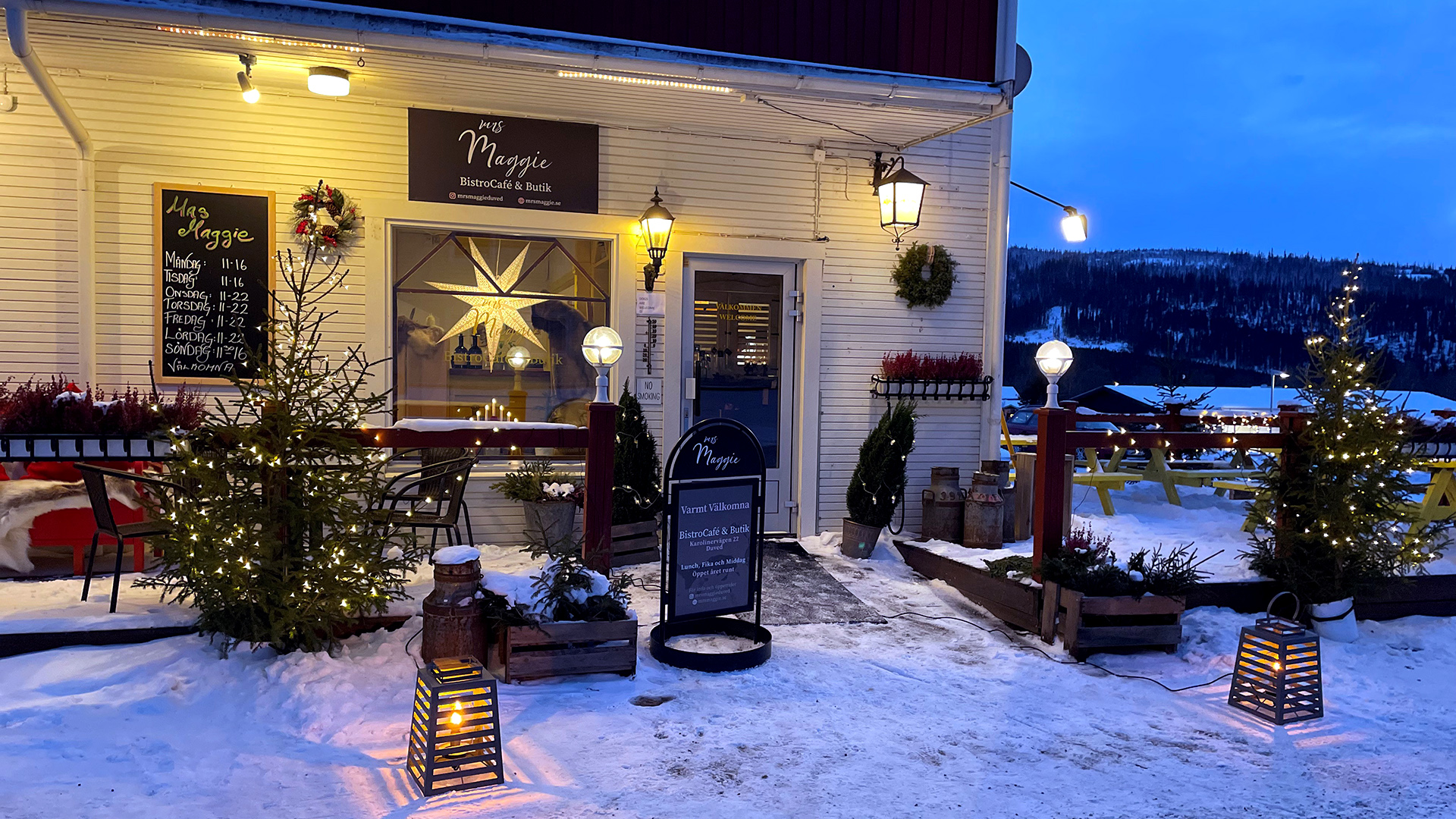 Bistro i vintermiljö med juldekorationer, upplyst fasad och snölandskap, kvällstid i Sverige