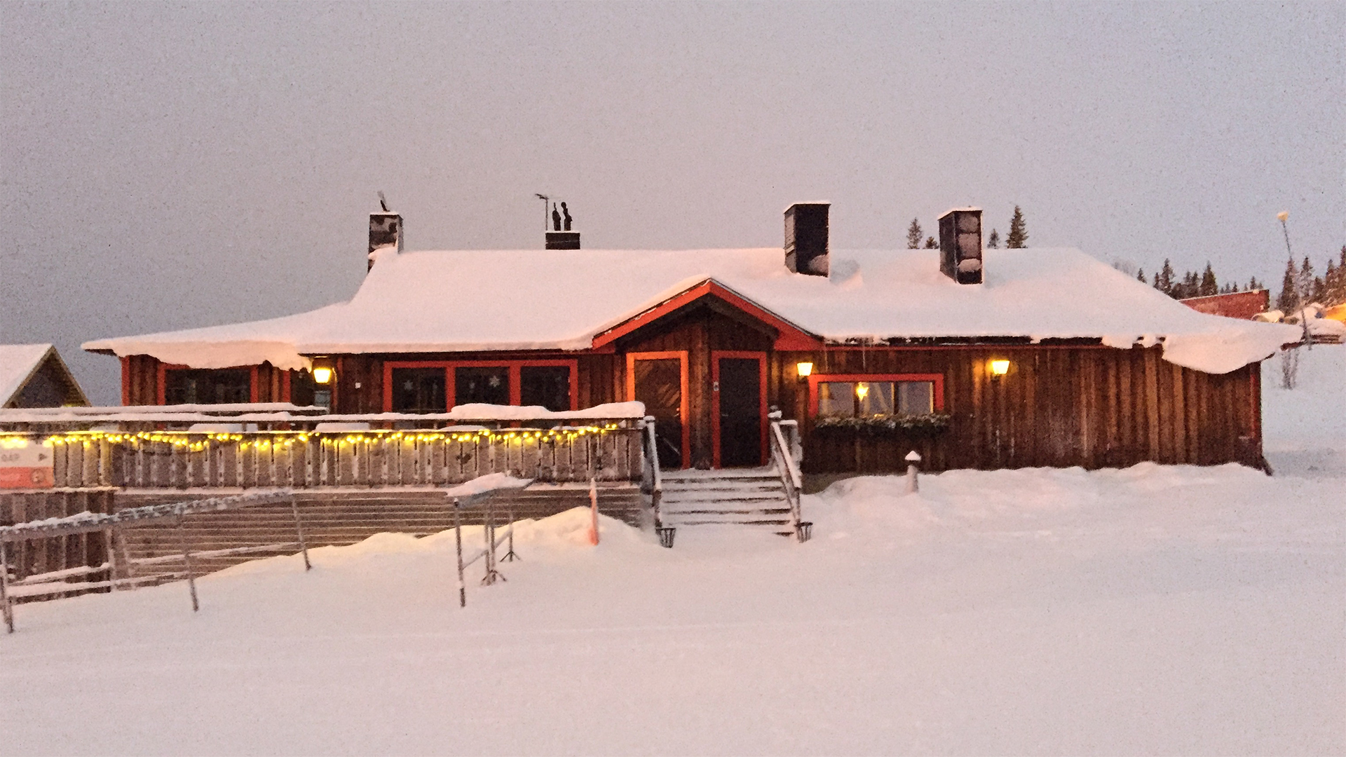 Snötäckt fjällstuga i Sverige, omgiven av träd och belysning, under vintertid