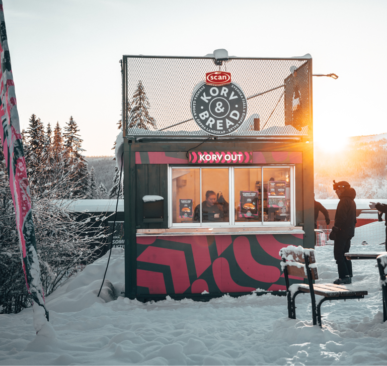 Korvstand im Winterlandschaft mit schneebedecktem Boden und Bäumen im Hintergrund, Sonnenuntergang am Horizont
