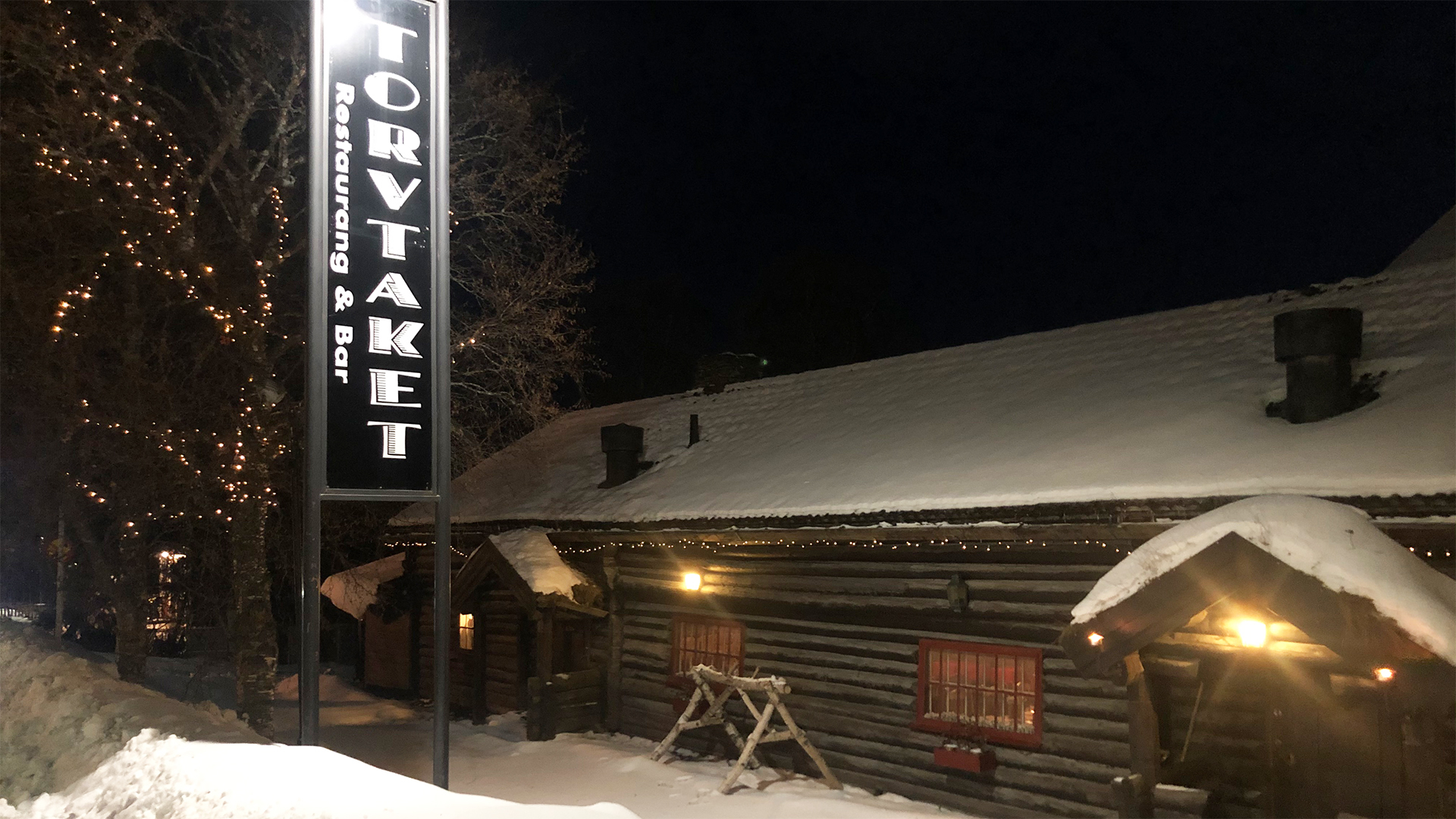 Schneebedecktes Blockhaus mit Schild für Torvtaket Restaurant & Bar, abends