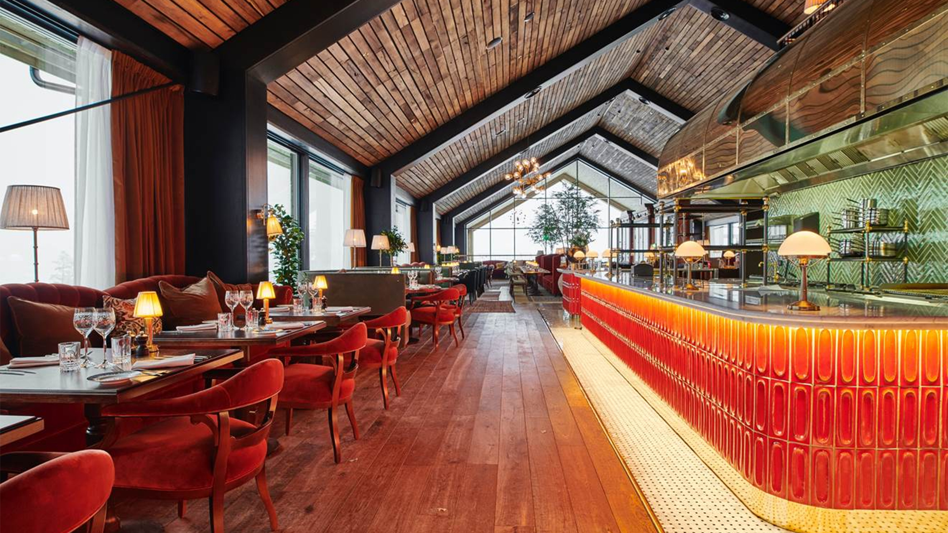 Restauranginteriör med träpaneler i taket, röda stoppade stolar, eleganta bord och en stämningsfull belysning vid en stilfull bardisk