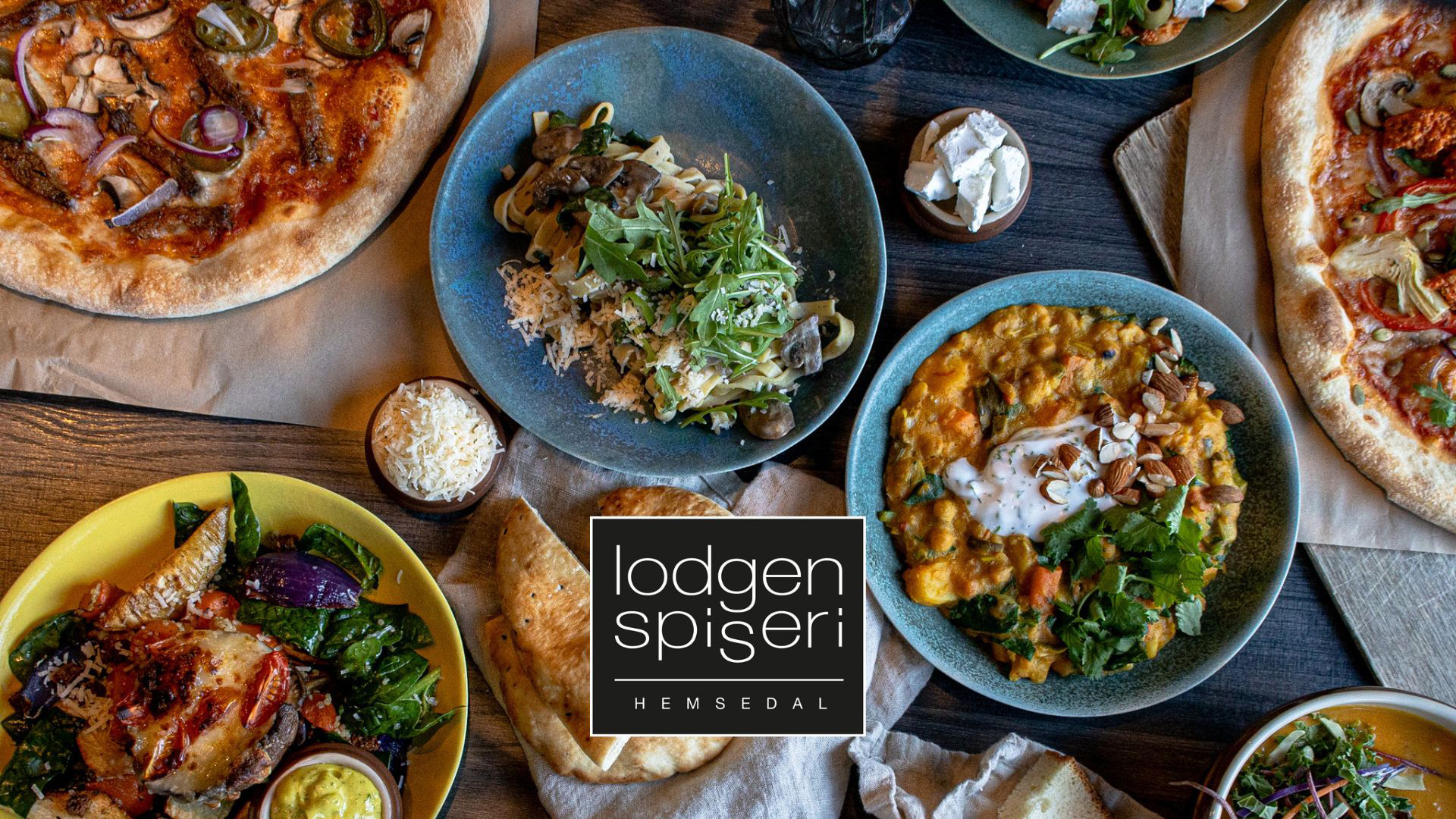 En mängd olika rätter från Lodgen Spiseri i Hemsedal, inklusive pizza, sallad, och gryta, placerade på ett bord
