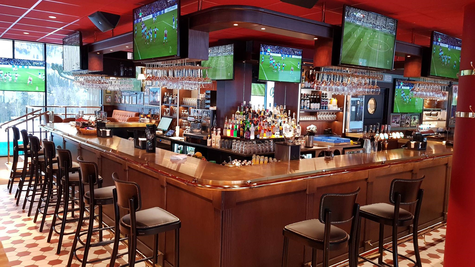 Modern sportbar med flera TV-skärmar som visar fotbollsmatcher, elegant träbar med barstolar och ett brett urval av drycker