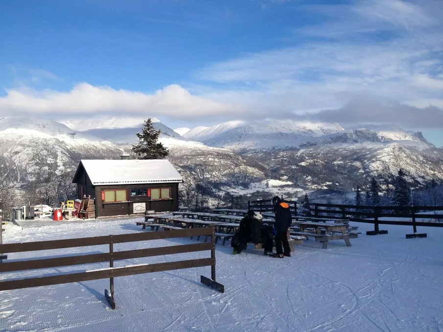 Fjällandskap med snöbeklädda berg, en stuga och människor på en vinterresort