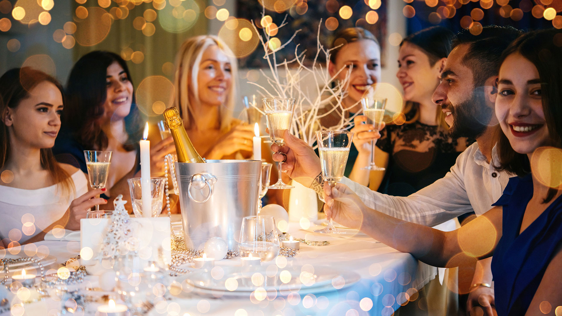 Personer som firar vid ett festligt middagsbord, skålar med champagneglas omgivna av ljus och dekorationer