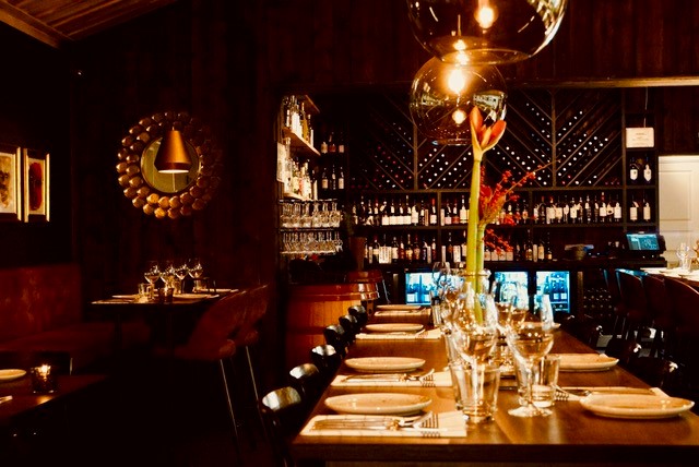 Stämningsfull interiör av en elegant restaurang med dämpad belysning, väl dukade bord och en vinvägg i bakgrunden