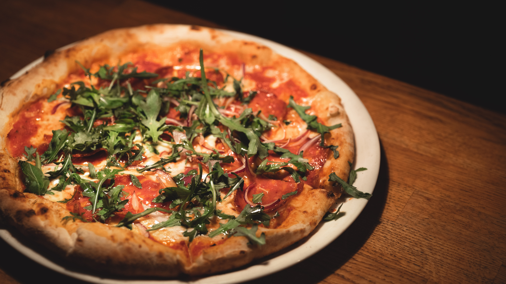 Vedugnsbakad pizza med tomatsås, mozzarella, skinka och ruccola på en vit tallrik