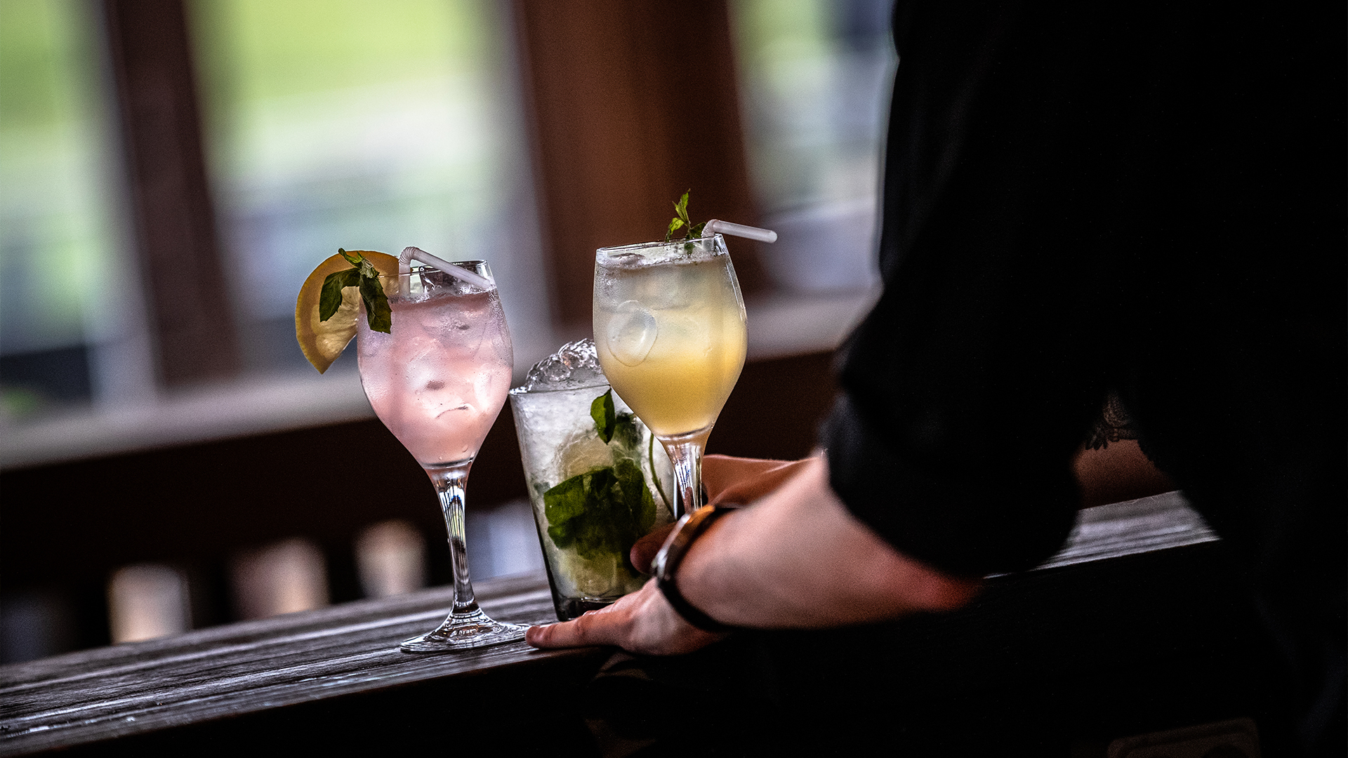 Tre somriga cocktails på rad med färgglada drycker och garneringar på en träbar