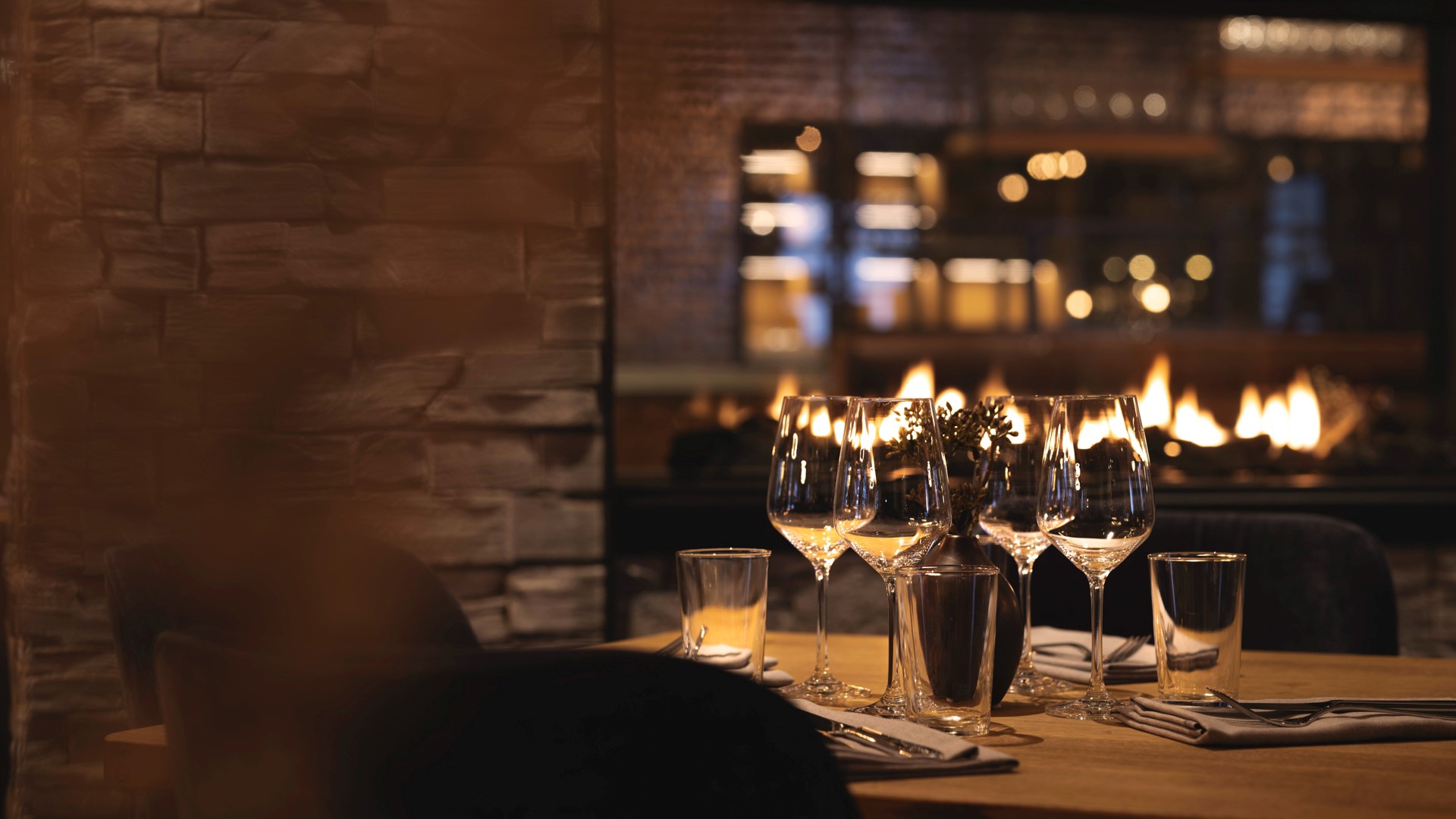 Elegant restauranginteriör med ett dukat bord, vinglas och en brasa i bakgrunden. Harmonisk atmosfär med stämningsfull belysning