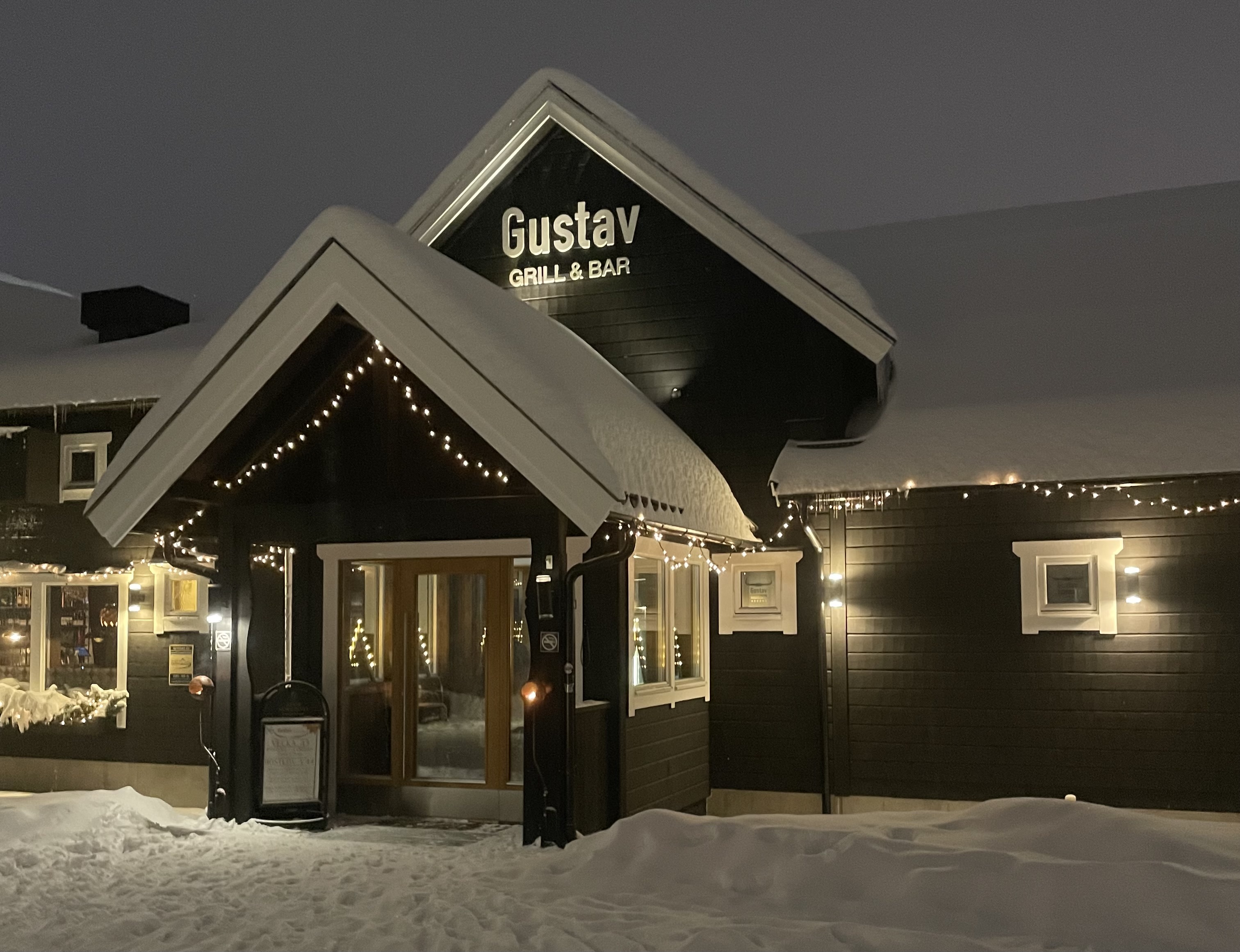 Restaurang exteriör av Gustav Grill & Bar i vinterlandskap med snö och dekorativa ljusslingor