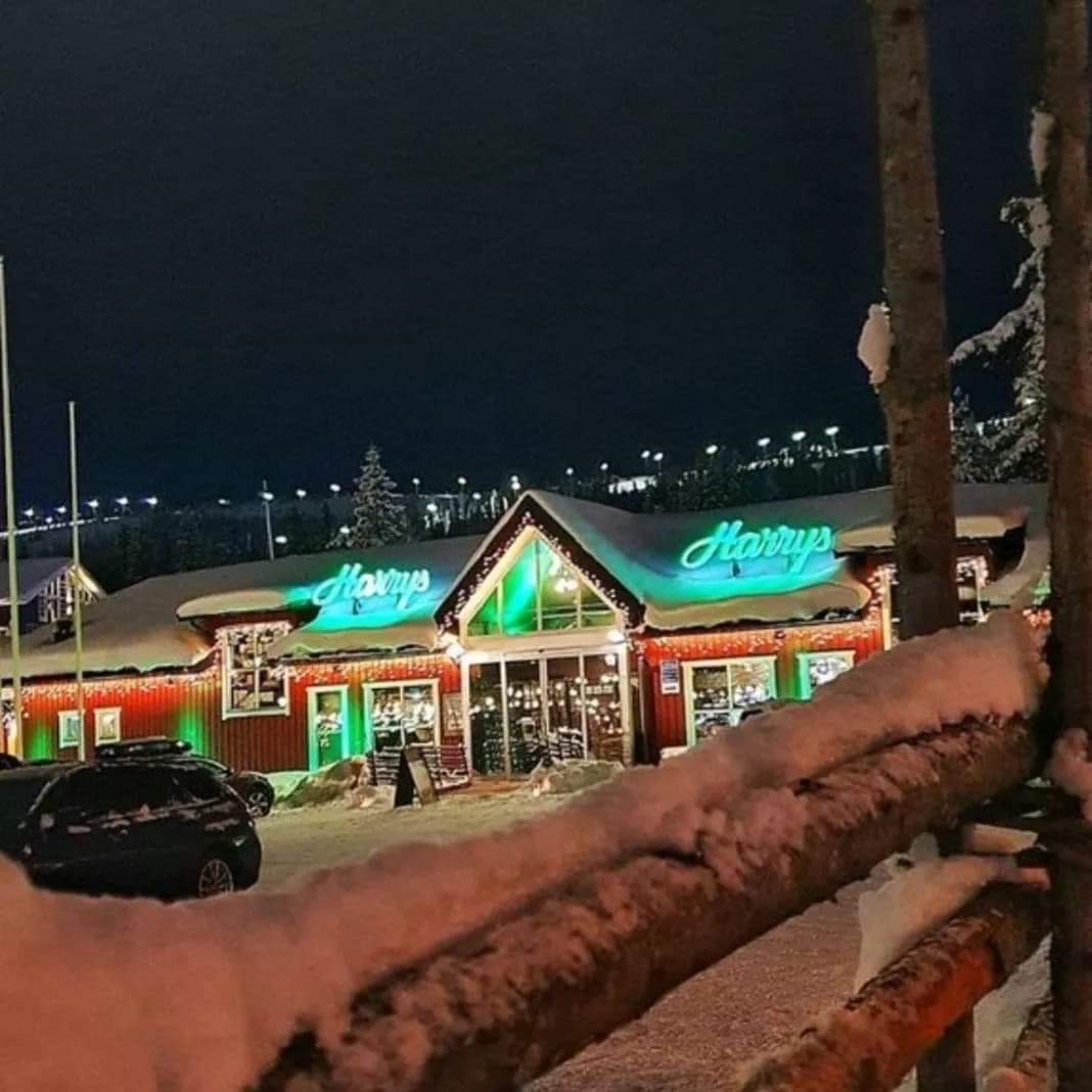 Röd träbyggnad med neonskylt under vinterkväll, inramad av snötäckta träd, ger en idyllisk och mysig atmosfär