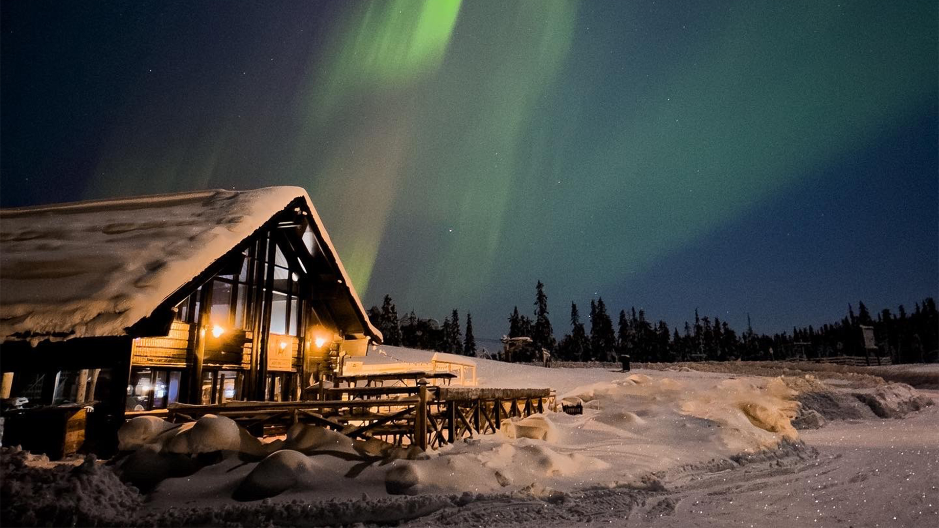 Snötäckt stuga under norrsken i norra Sverige, med klart nattlandskap och stjärnklar himmel
