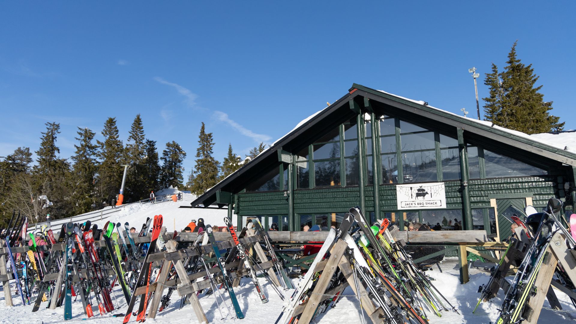 Skidutrustning utanför en stuga i ett vintrigt landskap, med skogar och klar blå himmel i bakgrunden