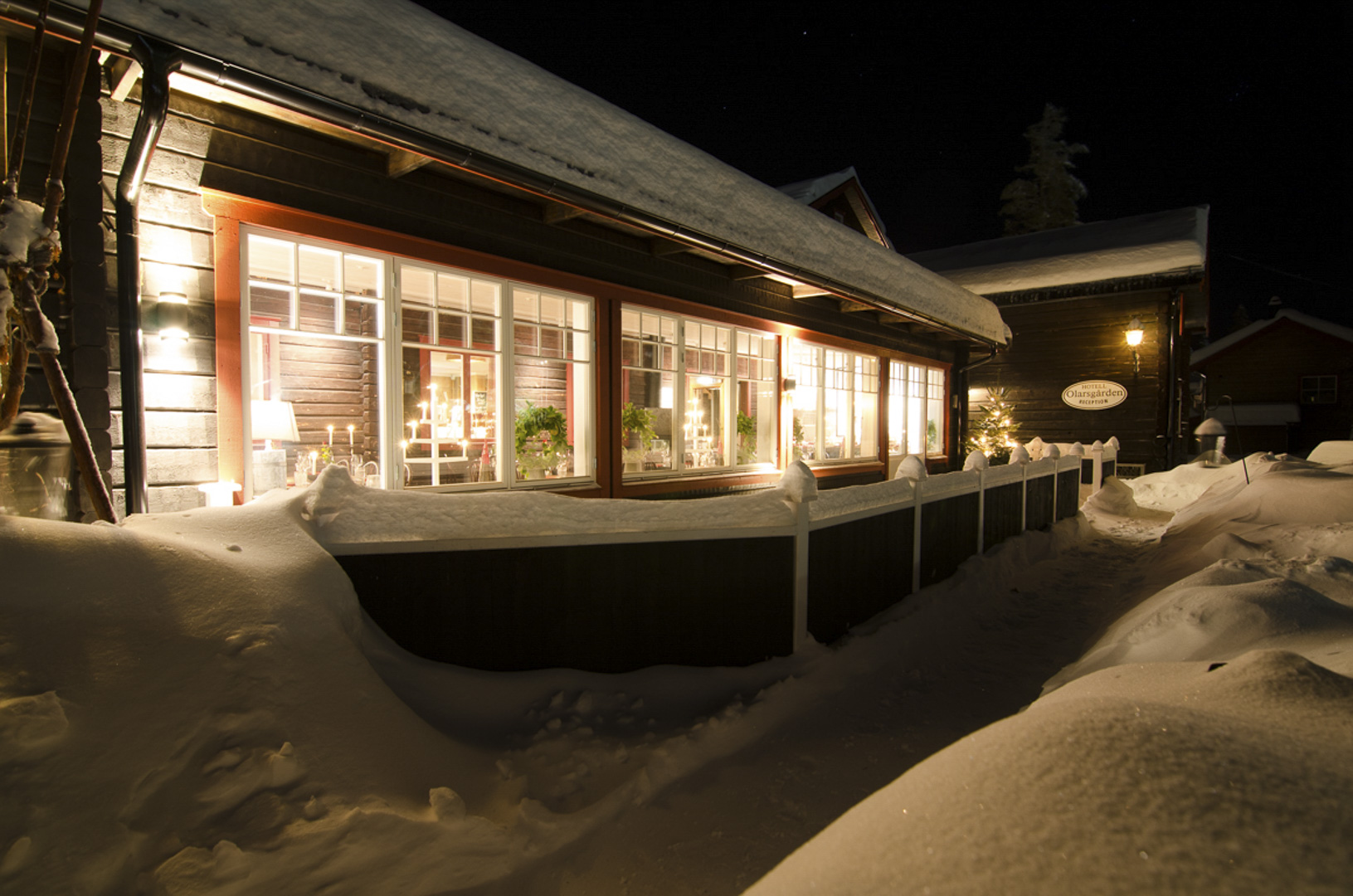 Snötäckt landskap runt belyst träbyggnad i Sverige under natten