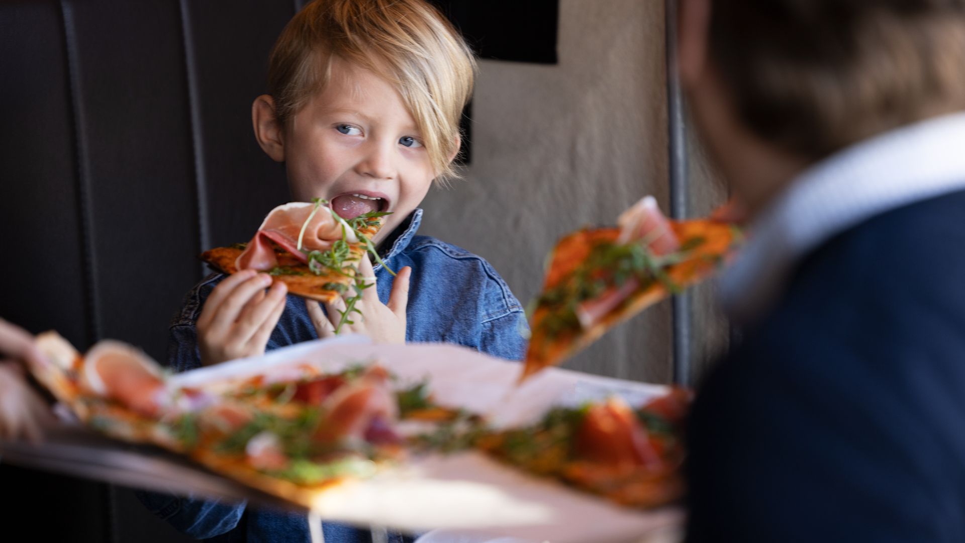 Pojke äter pizza med skinka och grönsaker i en restaurang