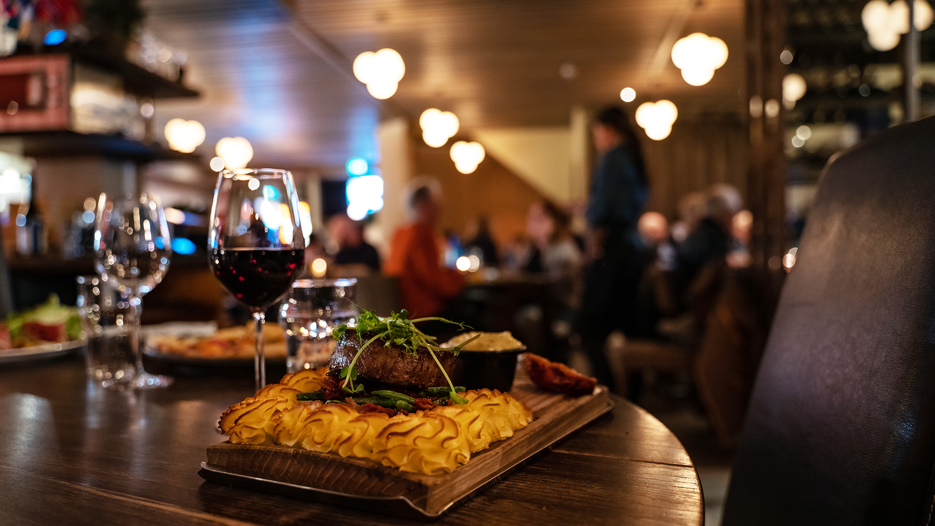 Gourmetmåltid med kött och potatisgratäng serveras på en restaurang, tillsammans med ett glas rött vin i en stämningsfull miljö