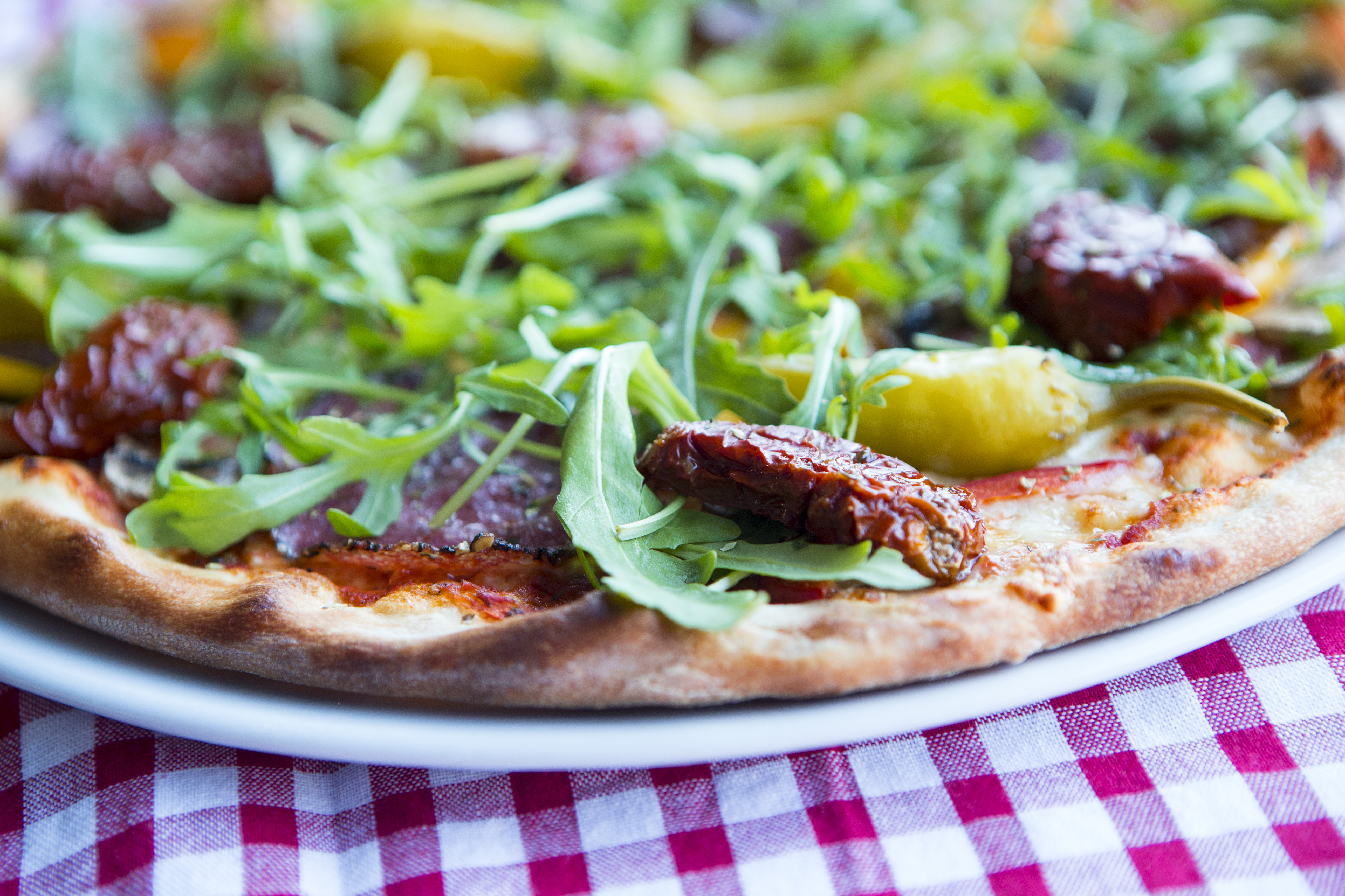 Pizza med rucola, soltorkade tomater och gul paprika på en rutigt duk