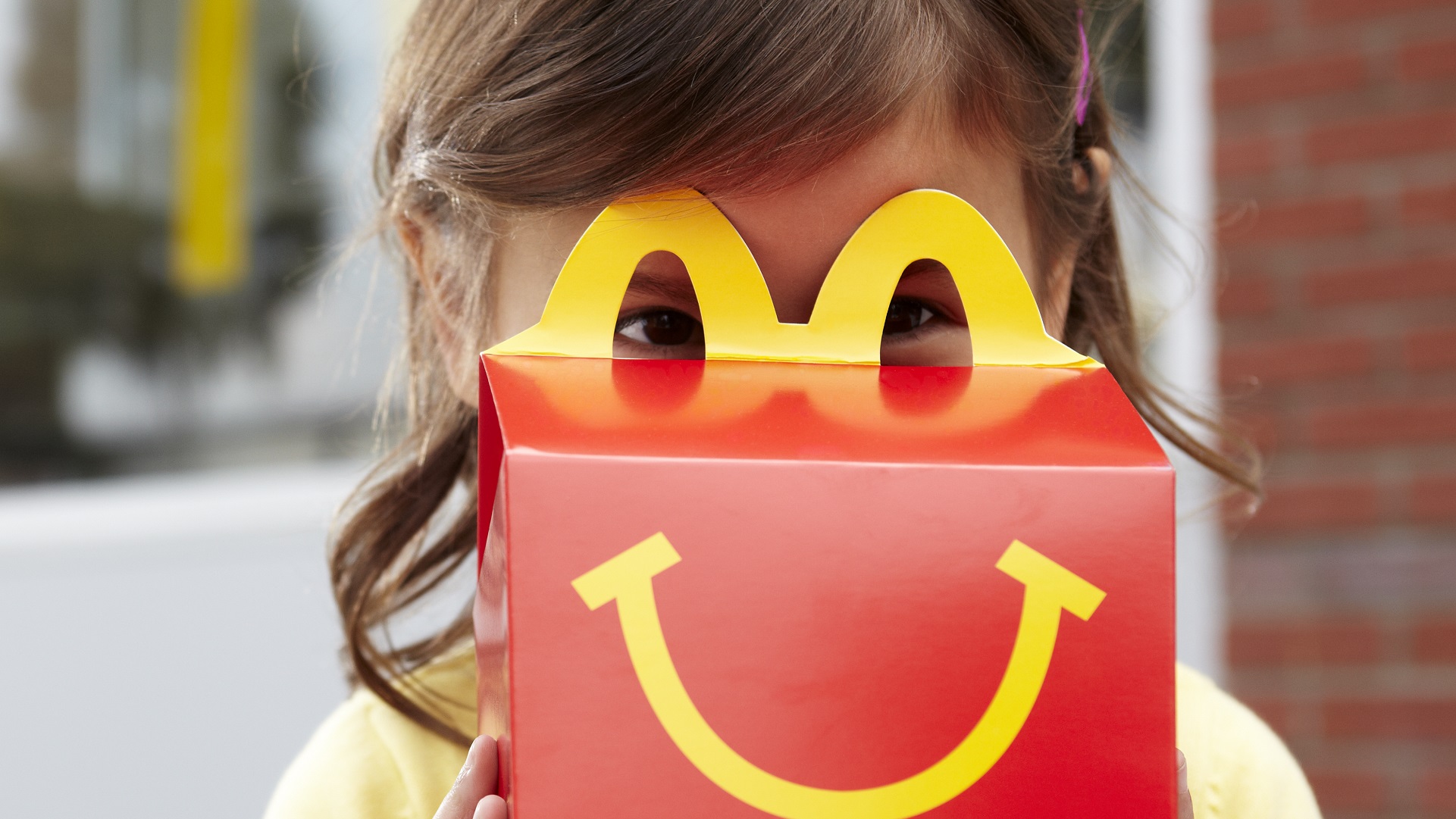 Flicka leker med McDonald's Happy Meal-låda utomhus