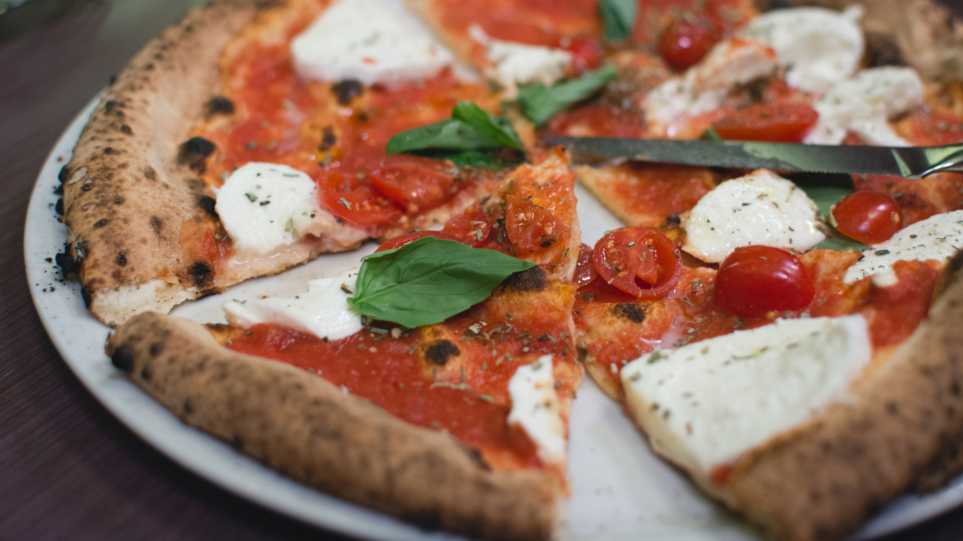 Napolitansk pizza med mozzarella, körsbärstomater och färsk basilika på en vit tallrik