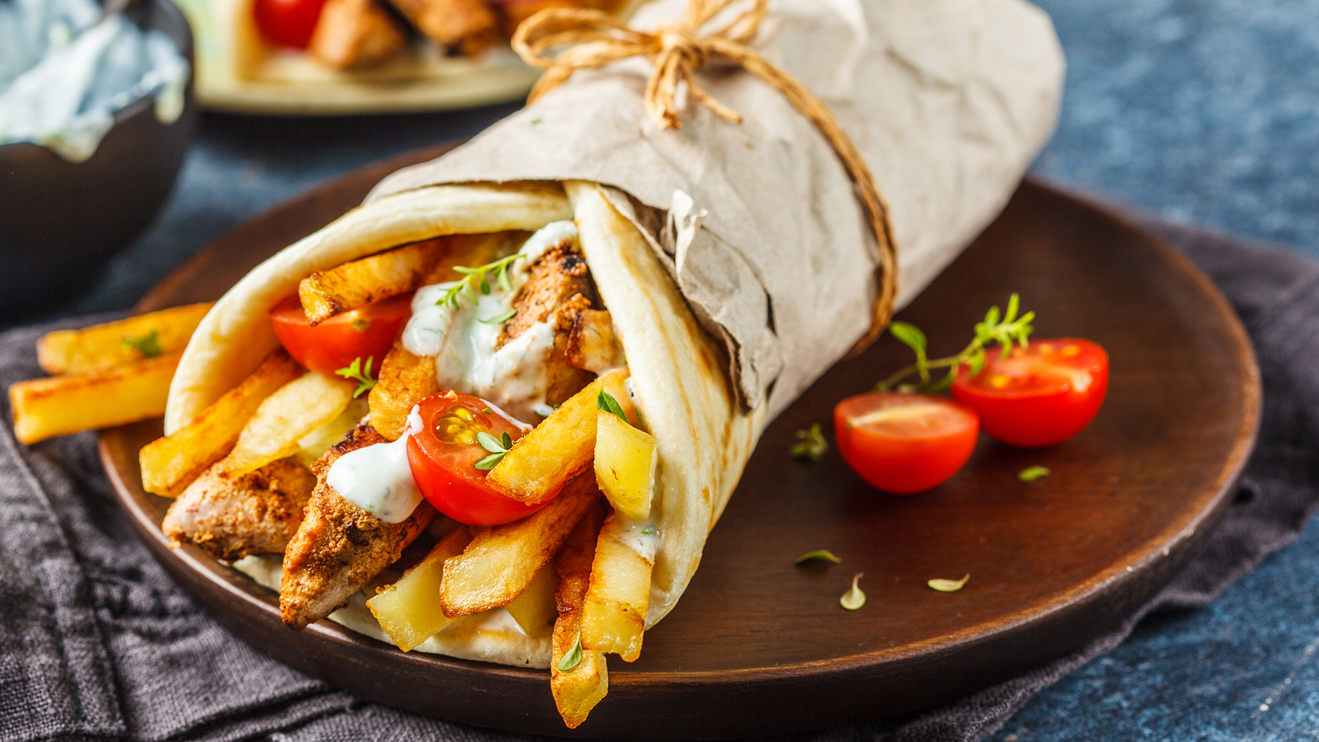 Gyros med grillat kött, pommes frites, körsbärstomater och sås inlindat i pitabröd på träfat