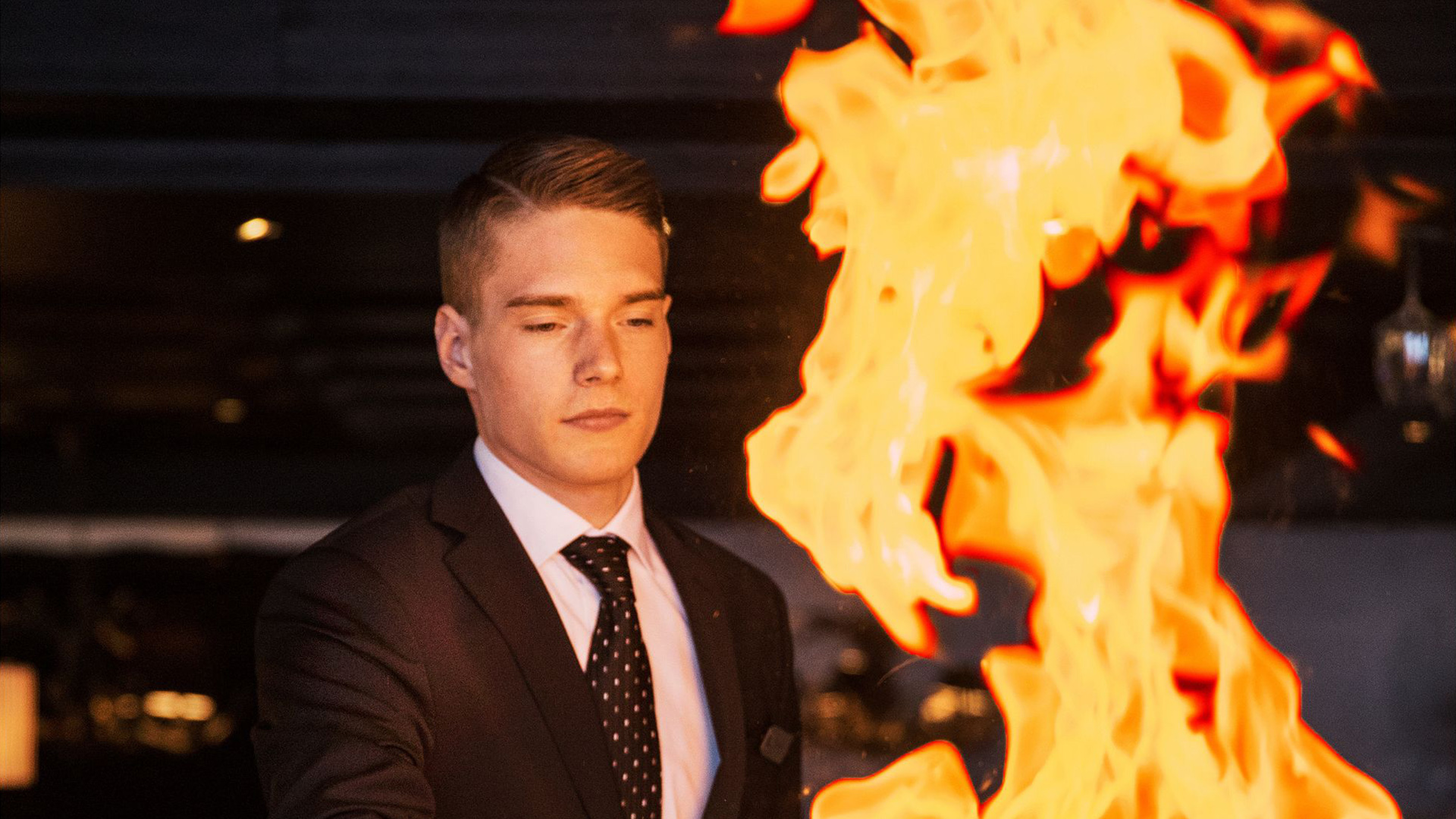 Man i kostym bredvid stora lågor i en mörk miljö