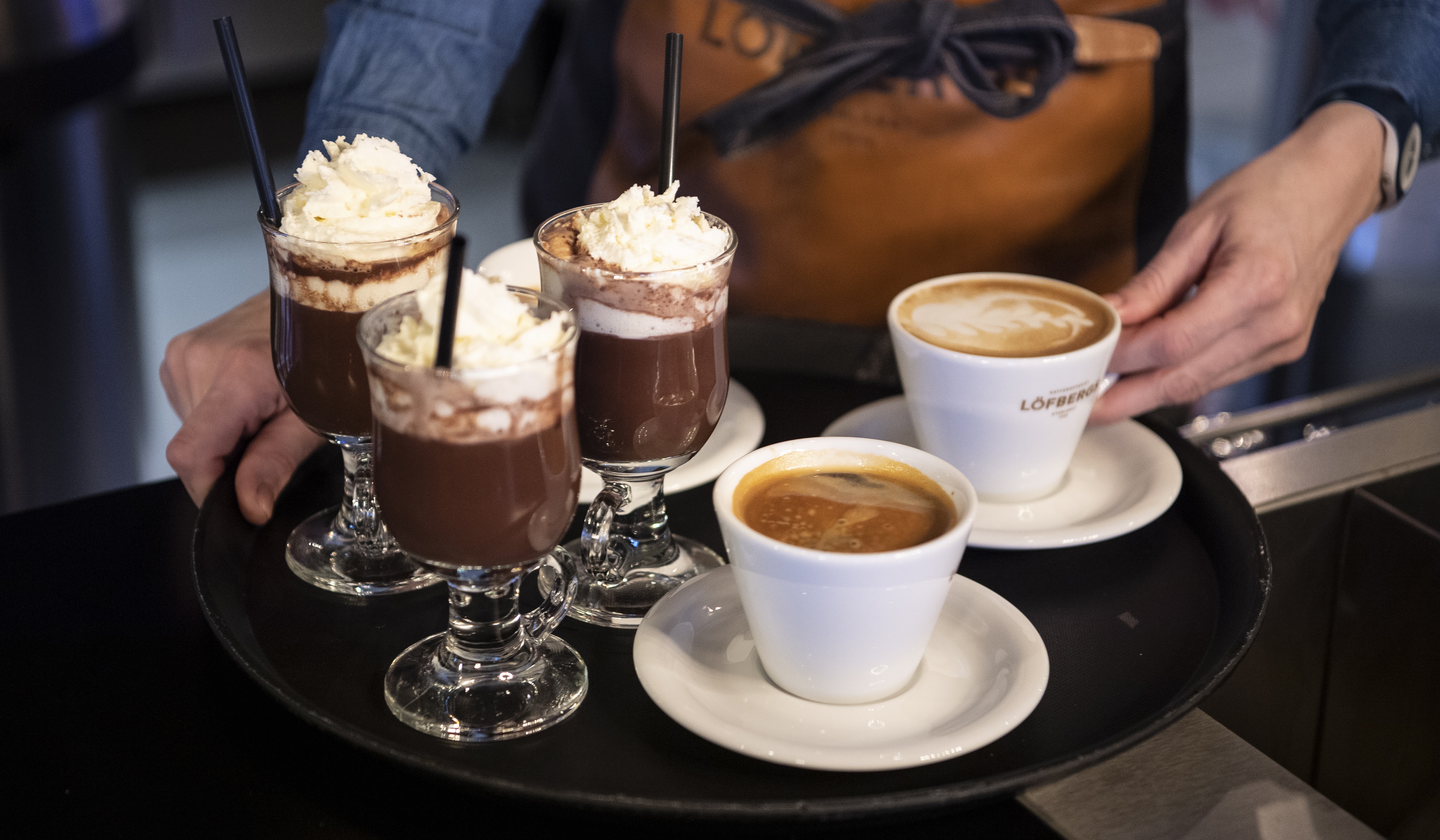 Serveringsbricka med varm choklad toppad med grädde och två koppar kaffe på ett kafé