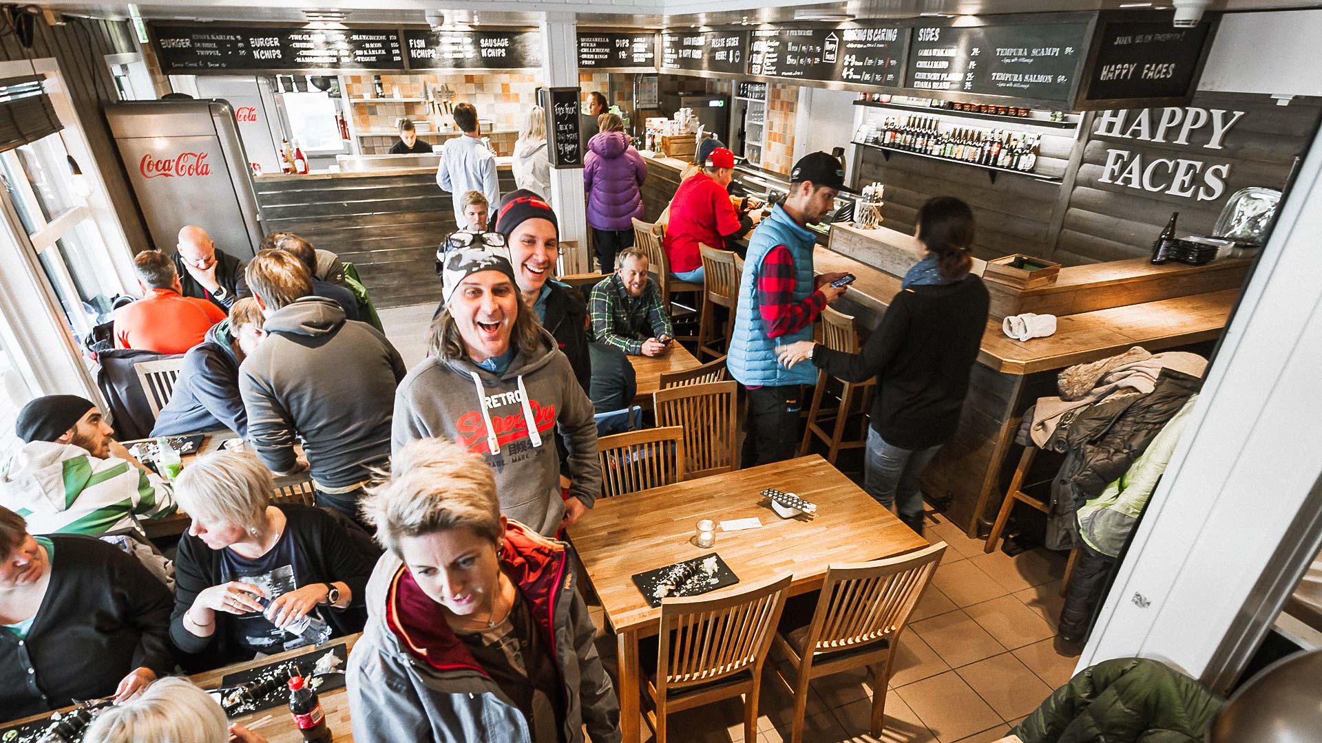 Människor umgås och äter i en livlig restaurangmiljö med träinredning och menyer på väggen