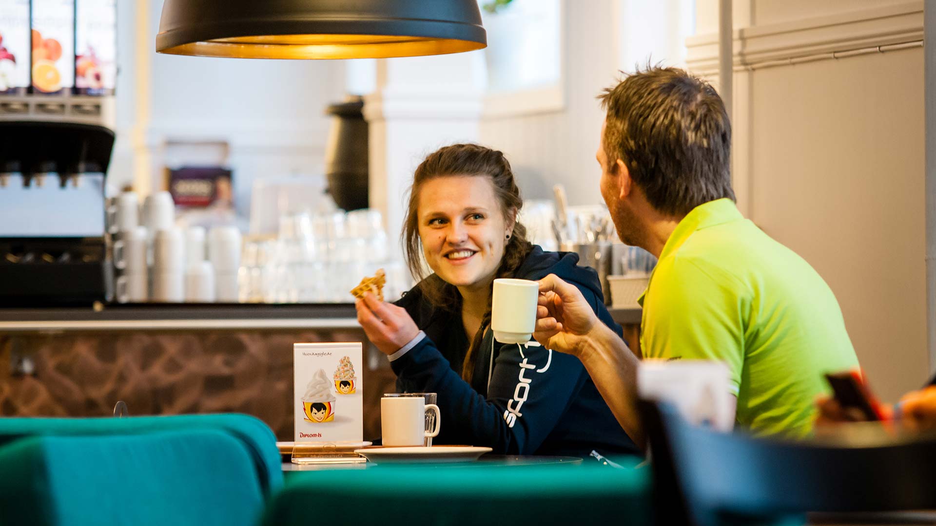 Personer sitter vid ett bord på ett kafé, dricker kaffe och äter bakverk, i en avslappnad och trivsam miljö