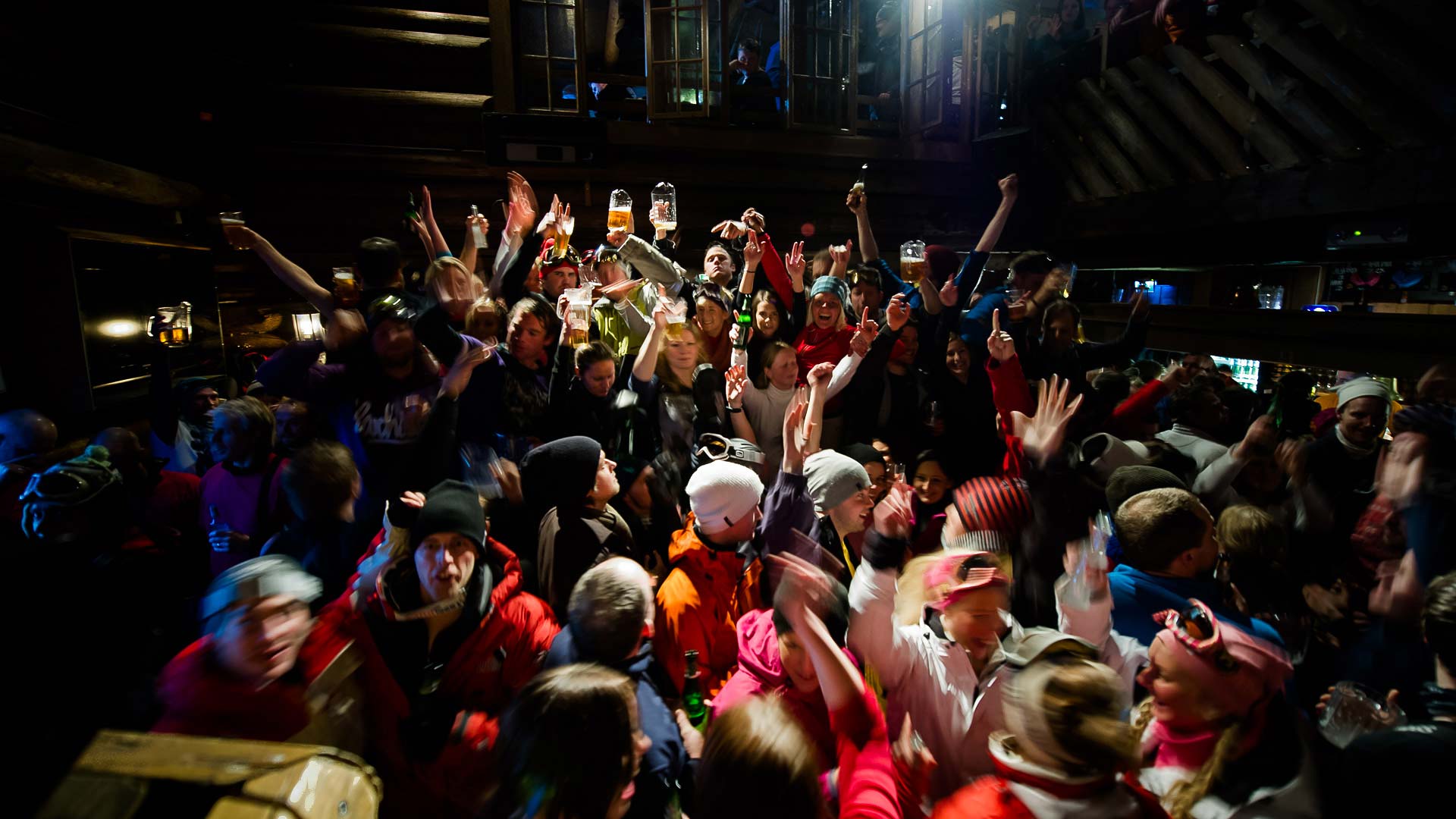 Människor dansar och firar på en livlig afterski-fest i en rustik alpstuga, omgivna av dunkla ljus och musik