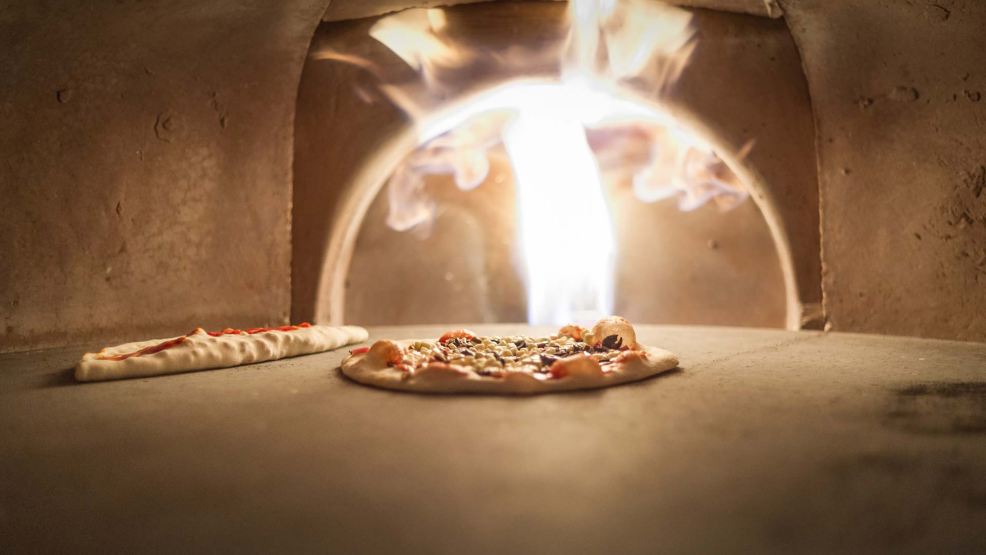 Vedeldad pizzaugn med glödande eld, där två pizzor bakas samtidigt