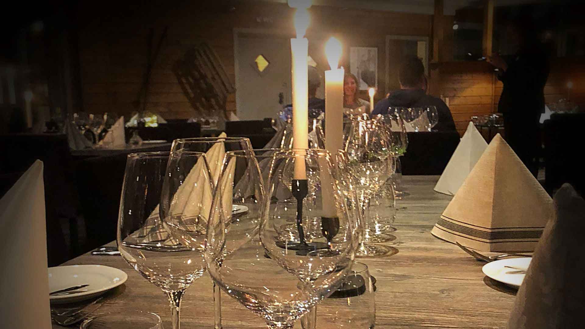 Dukning i restaurang med tända ljus, vinglas och vikta servetter på ett träbord i en mysig miljö