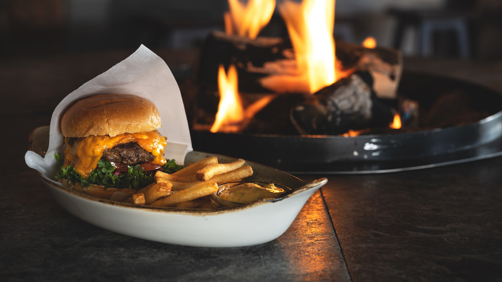 Hamburgare med cheddarost och pommes frites framför en brasa