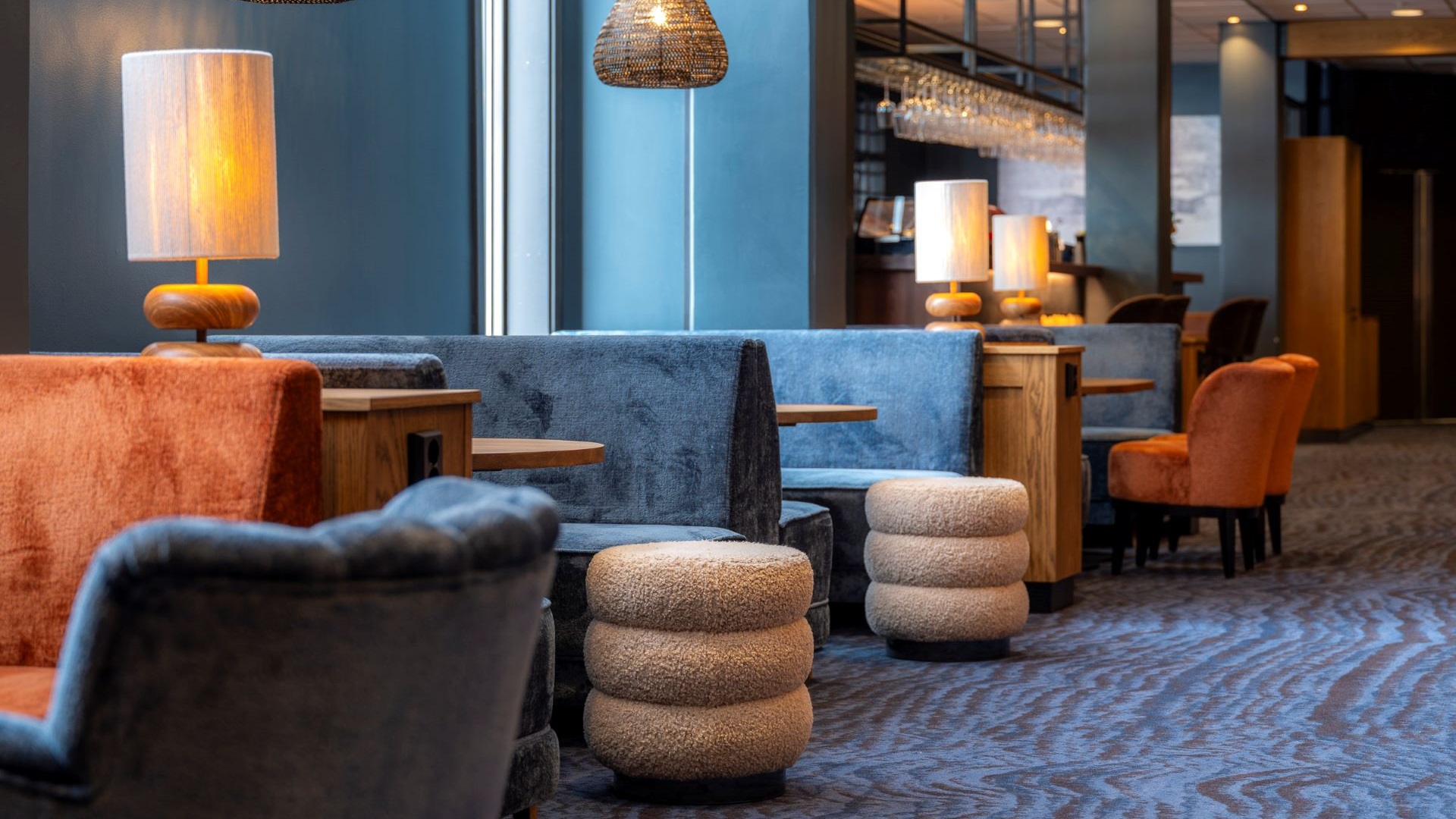 Modernt hotellobby med stilrena soffor och stolar i blå och orange nyanser, mjuka lampor och mönstrad matta