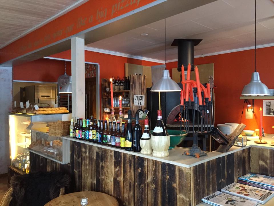 Pizzarestaurang med vedeldad ugn, rustik inredning och ölflaskor på baren