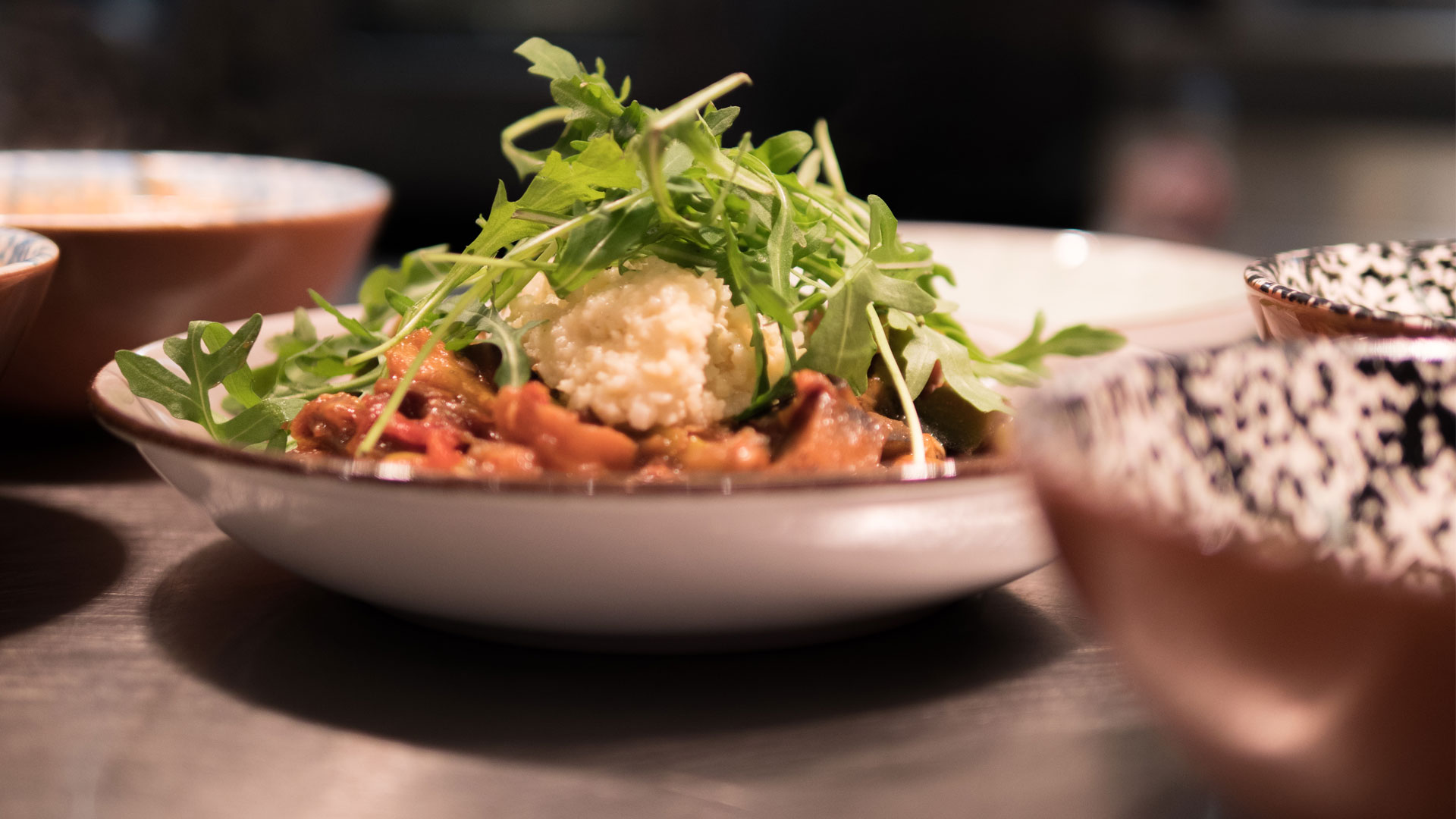 Vegetarisk rätt med rostade grönsaker och ris, toppad med färsk ruccola, serverad i en elegant skål på en restaurang