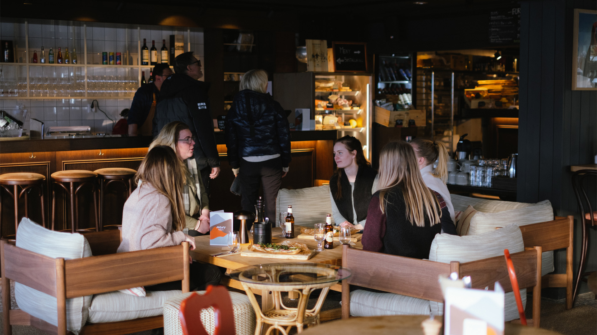 Personer samlade vid ett kafébord, njuter av drycker och samtal i en mysig miljö med bar i bakgrunden