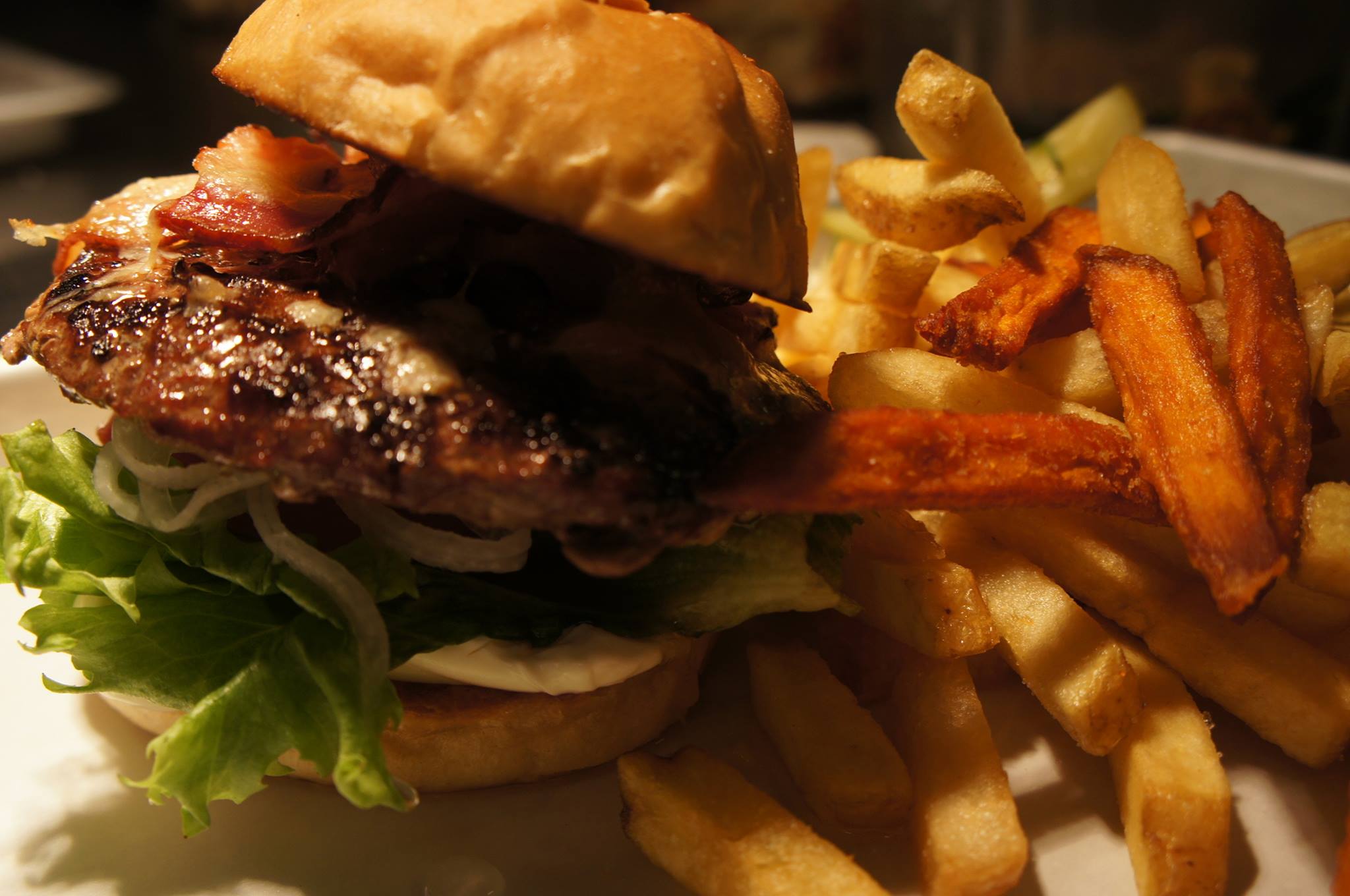 Saftig hamburgare med bacon och sallad på ett bröd, serverad med krispiga pommes frites