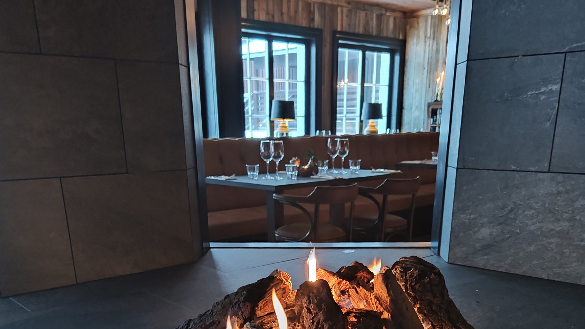 Öppen spis i elegant restaurangmiljö med uppdukade bord, bekväma sittplatser och mjuk belysning