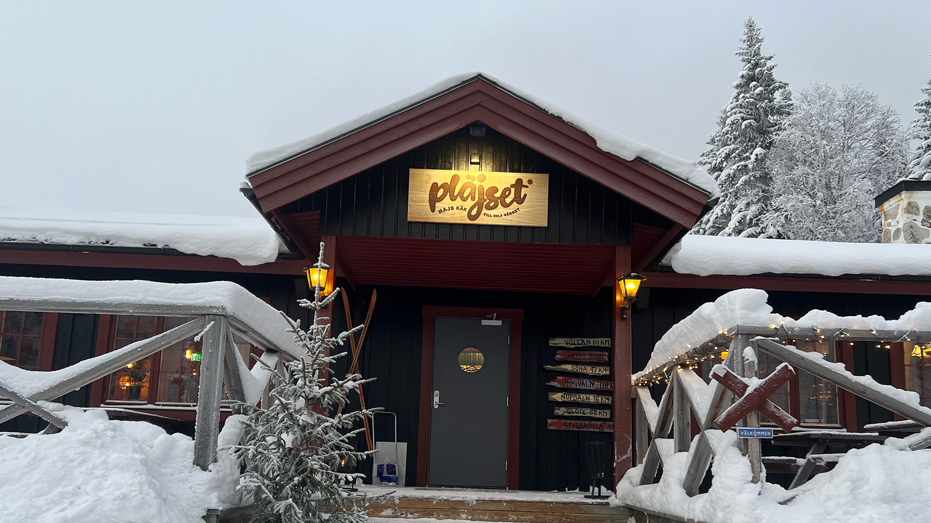 Snöklädd fjällrestaurant i Sverige med skylten "Pläjset" på fasaden, omgiven av vinterlandskap och granar