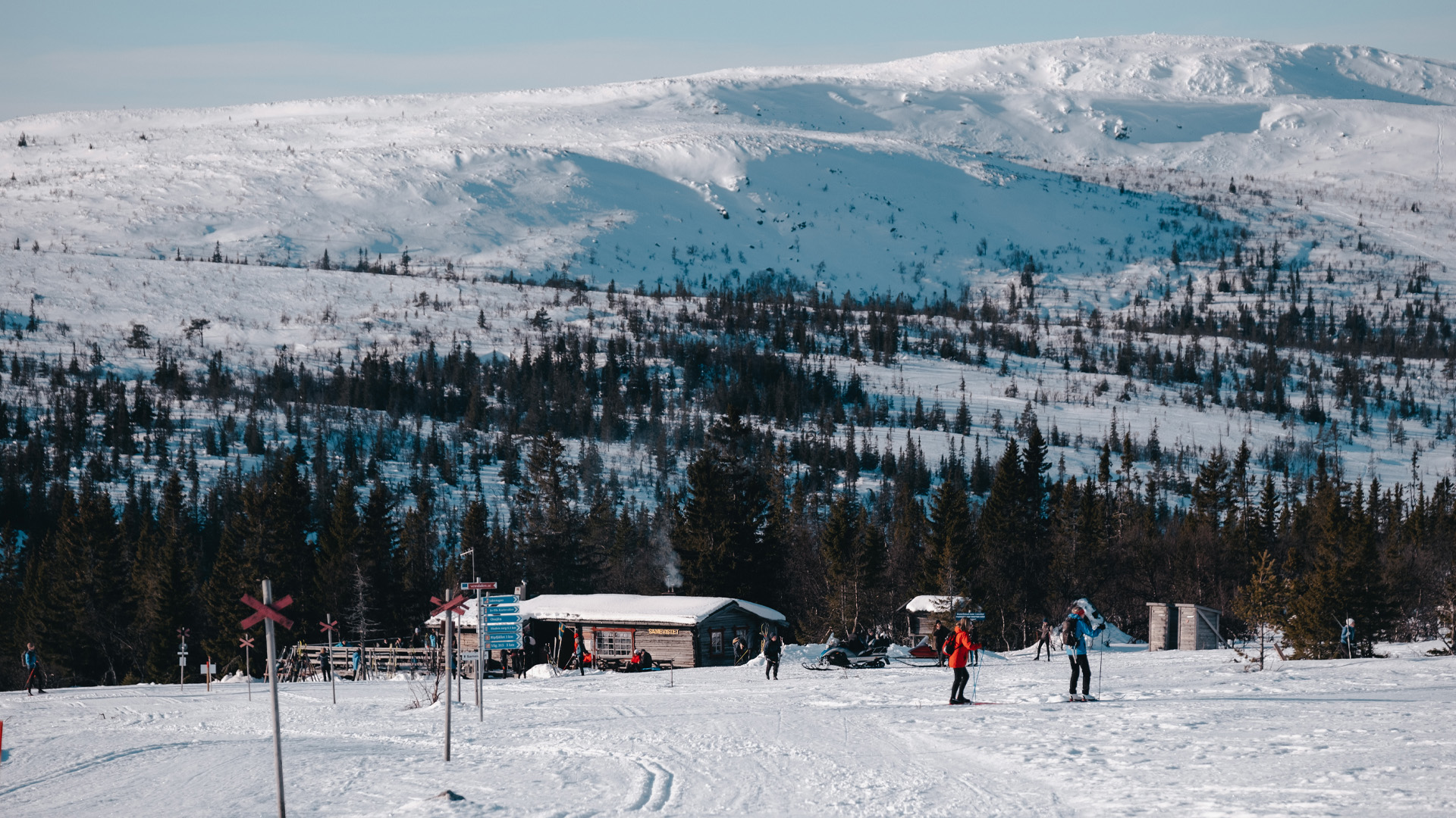 Vinterlandskap i svenska fjällen med snöklädda berg och skidåkare nära en stuga
