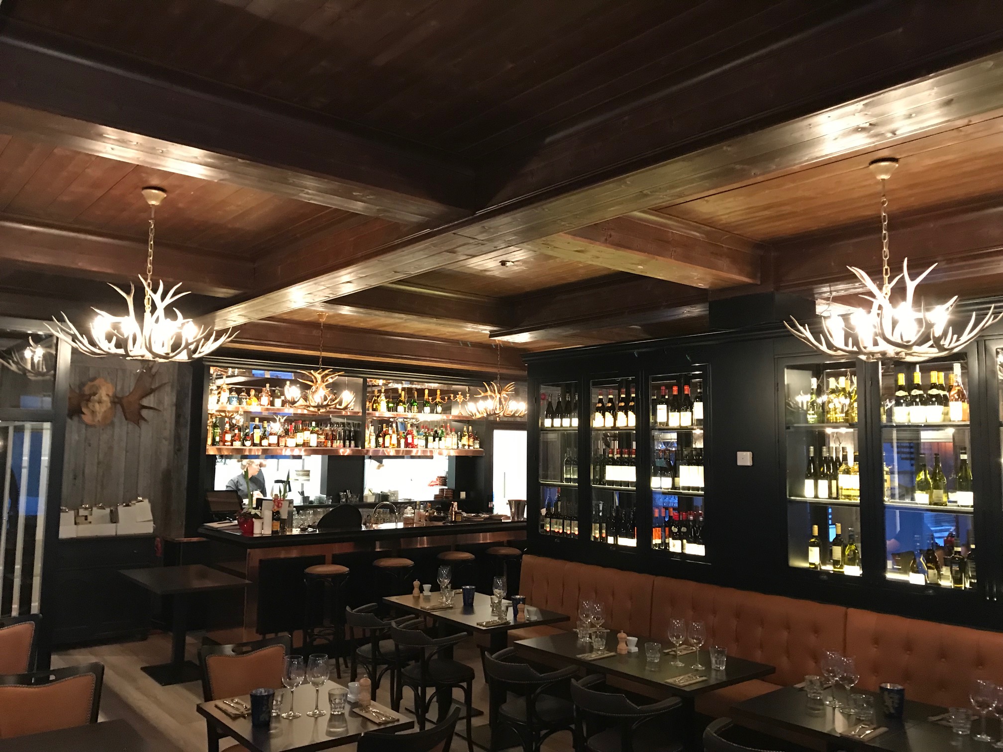 Restauranginteriör med träinredning, eleganta kandelabrar, välfylld bar och vinflaskor på hyllorna