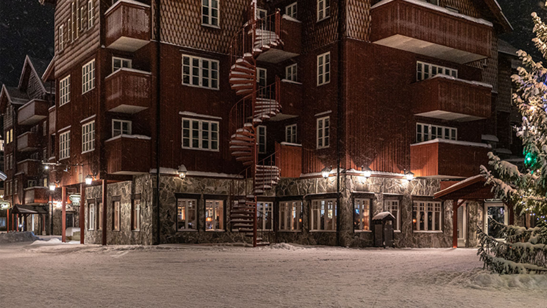 Rött flervåningshus med vinterdekorationer och snötäckta omgivningar i svenska fjällen på natten