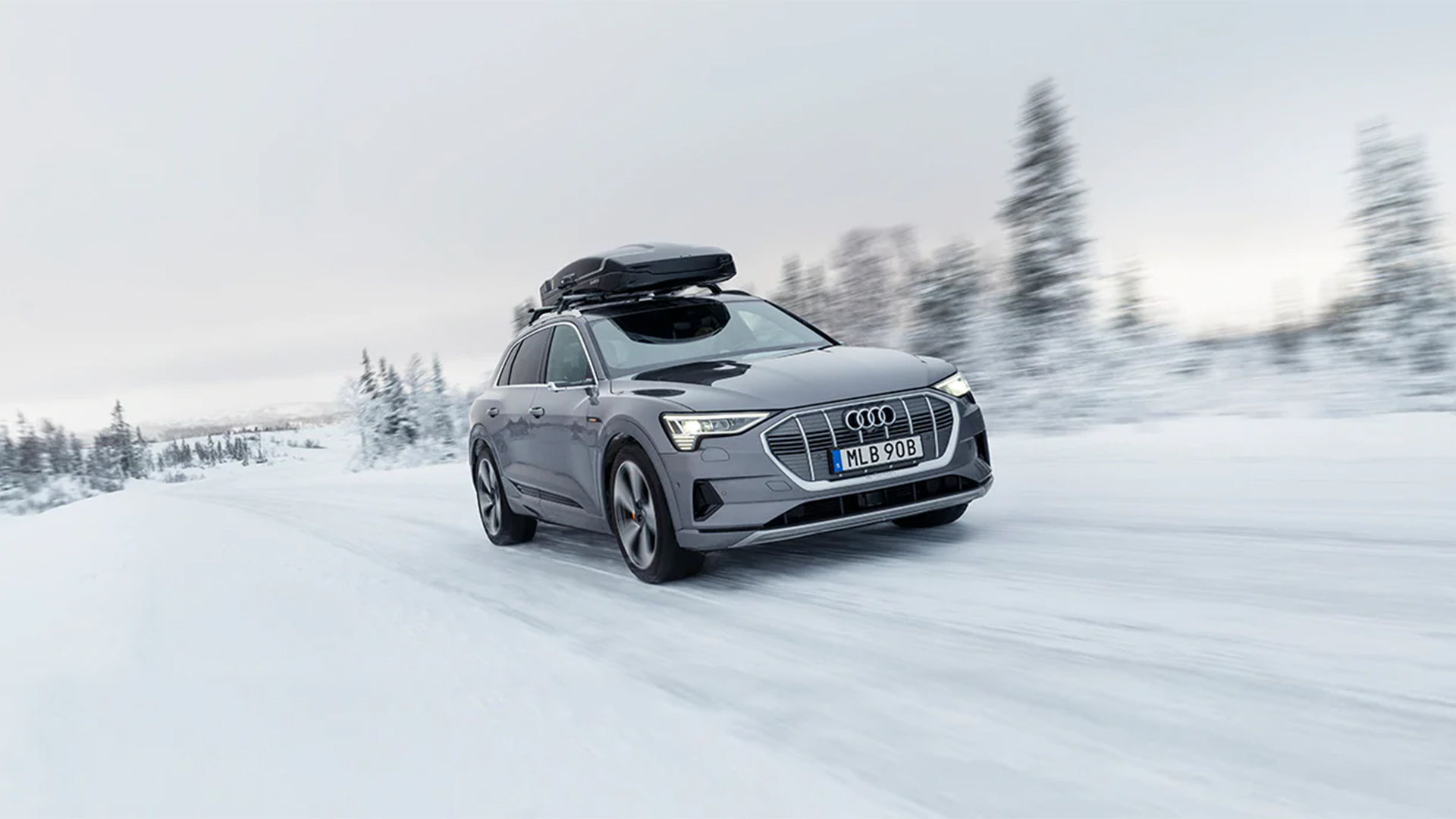 Elektrisk Audi e-tron kör på snöig väg med takbox i vintrigt landskap