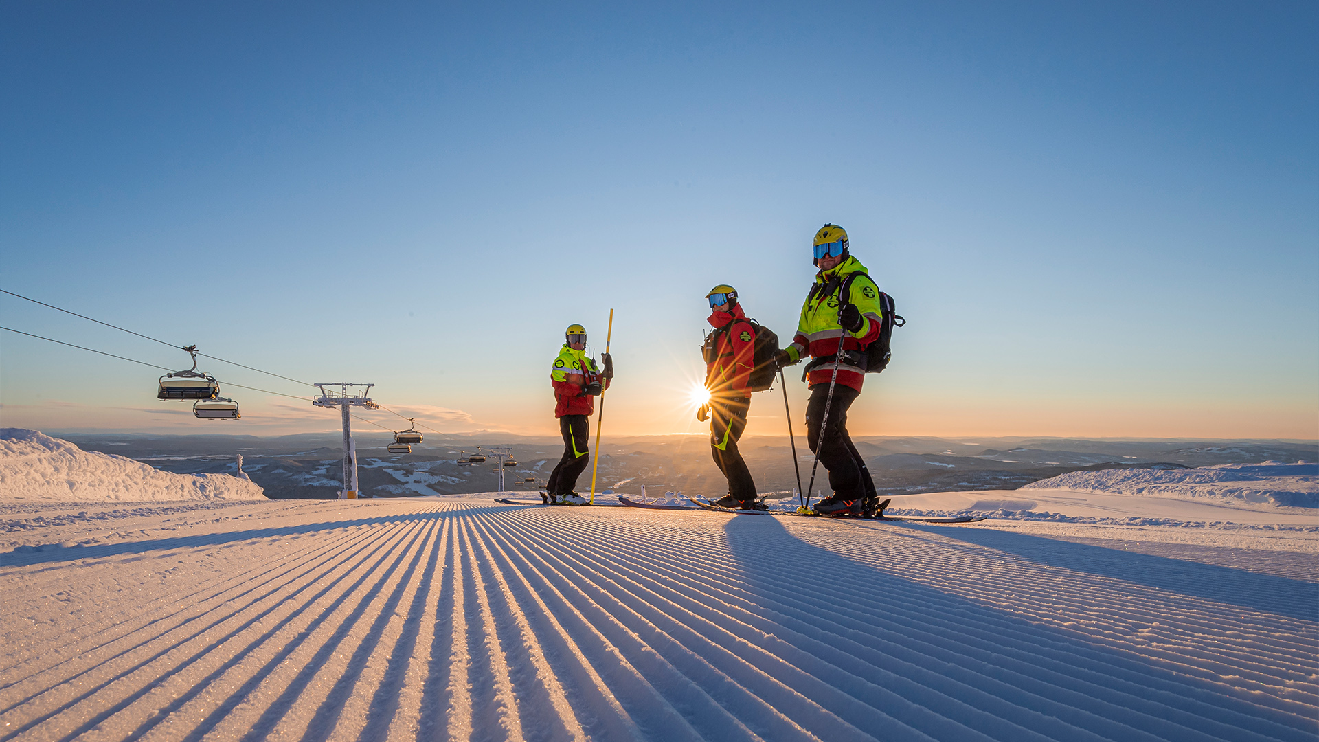 Skidpatrull på preparerad pist i solnedgång, fjälllandskap i Sverige med skidliftar i bakgrunden