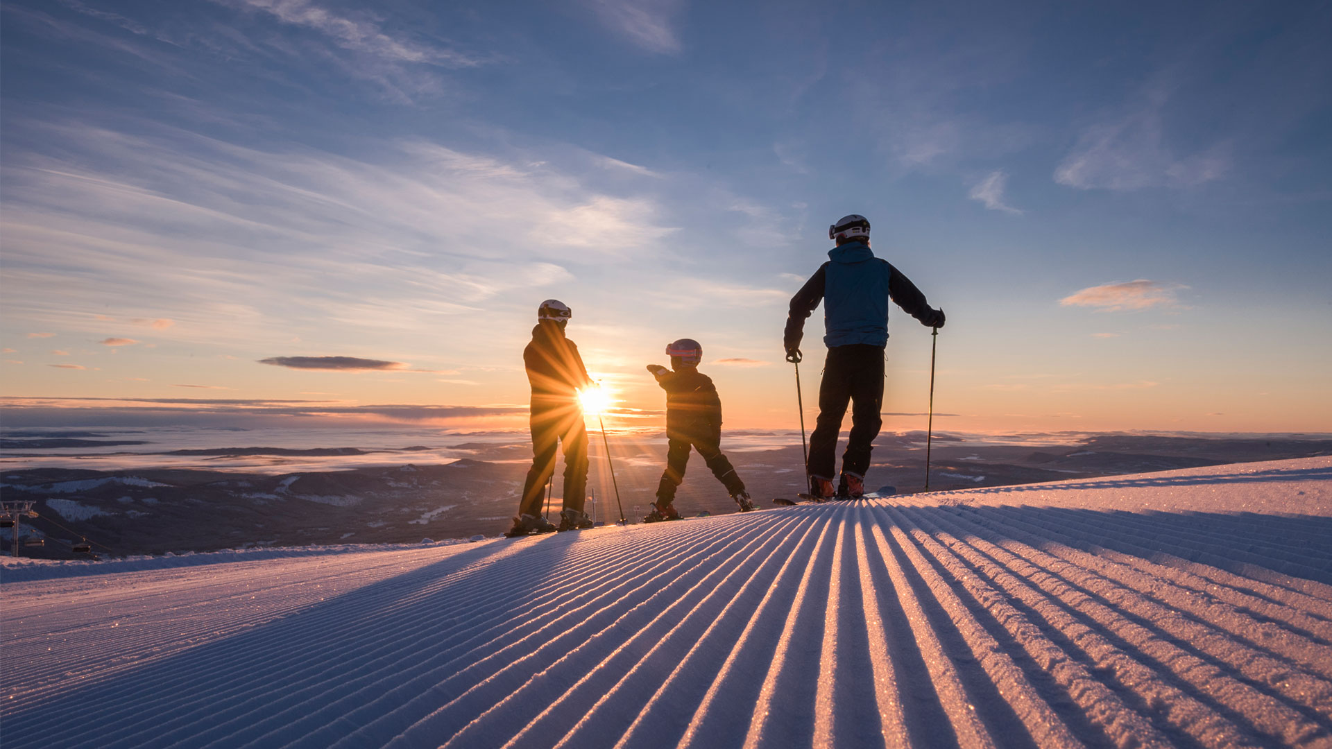 Skidåkare på en snötäckt backe vid solnedgång, med vidsträckt utsikt över fjällandskap i Sverige