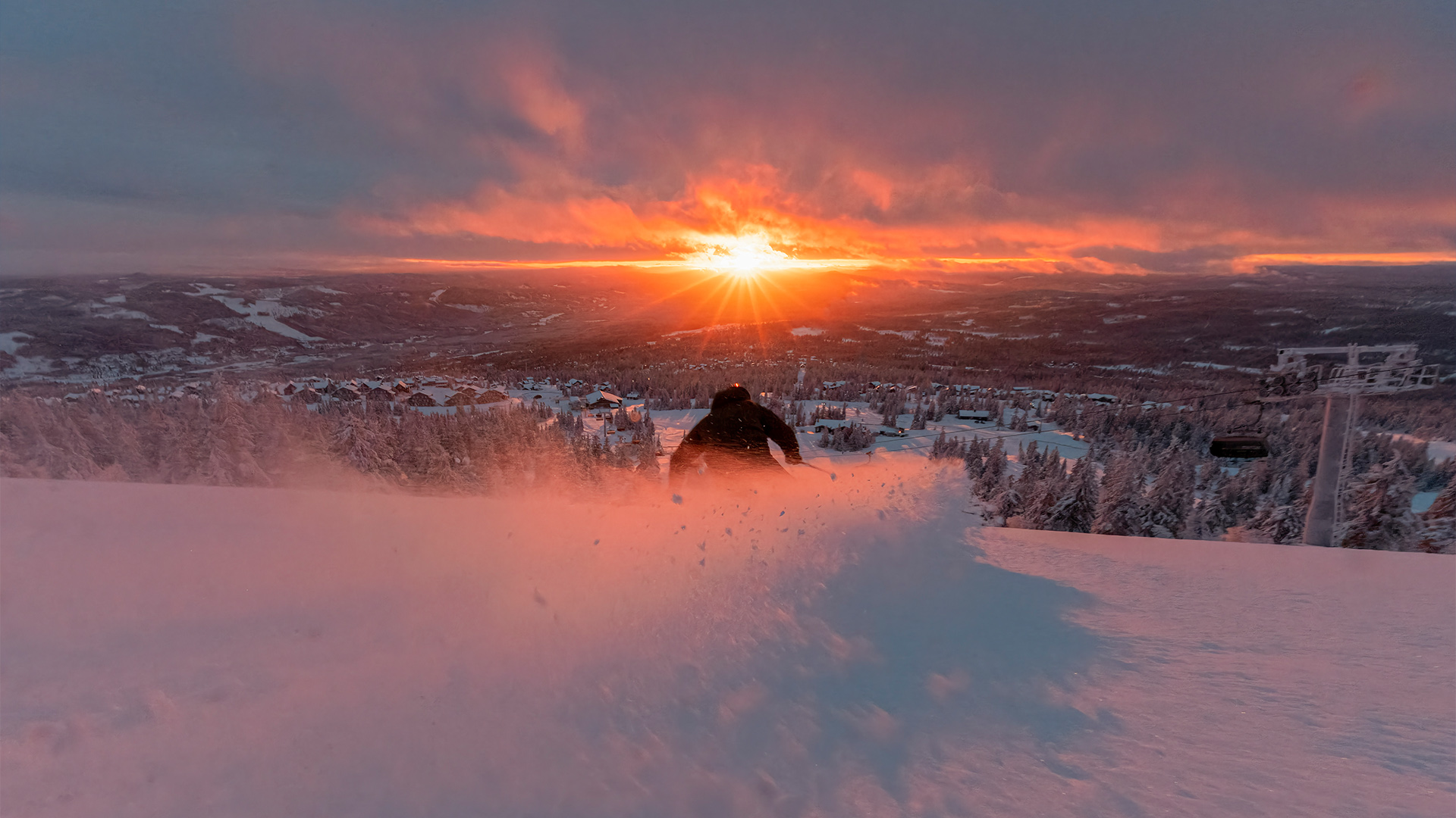 Solnedgång över snötäckta backar i skidort, person åker skidor nerför backen