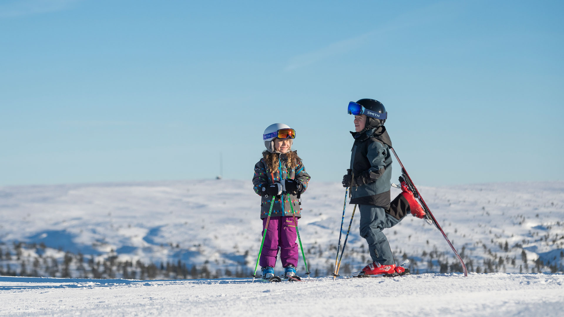 Two children skiing on a snowy mountain under a clear blue sky